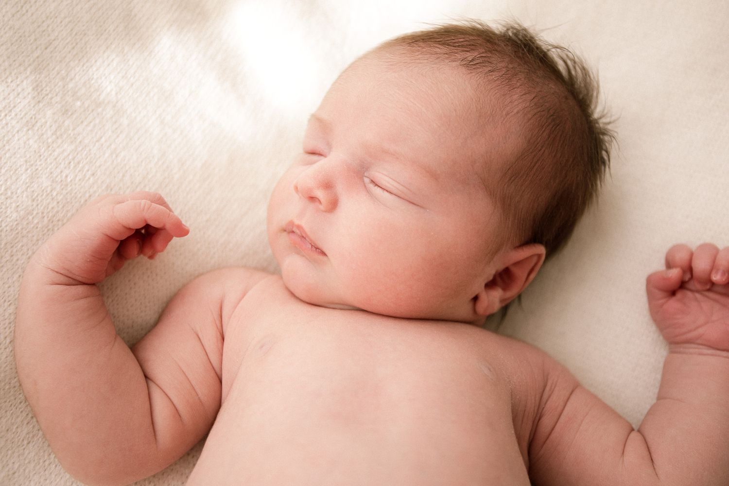 Serene newborn baby sleeping on white textured background.