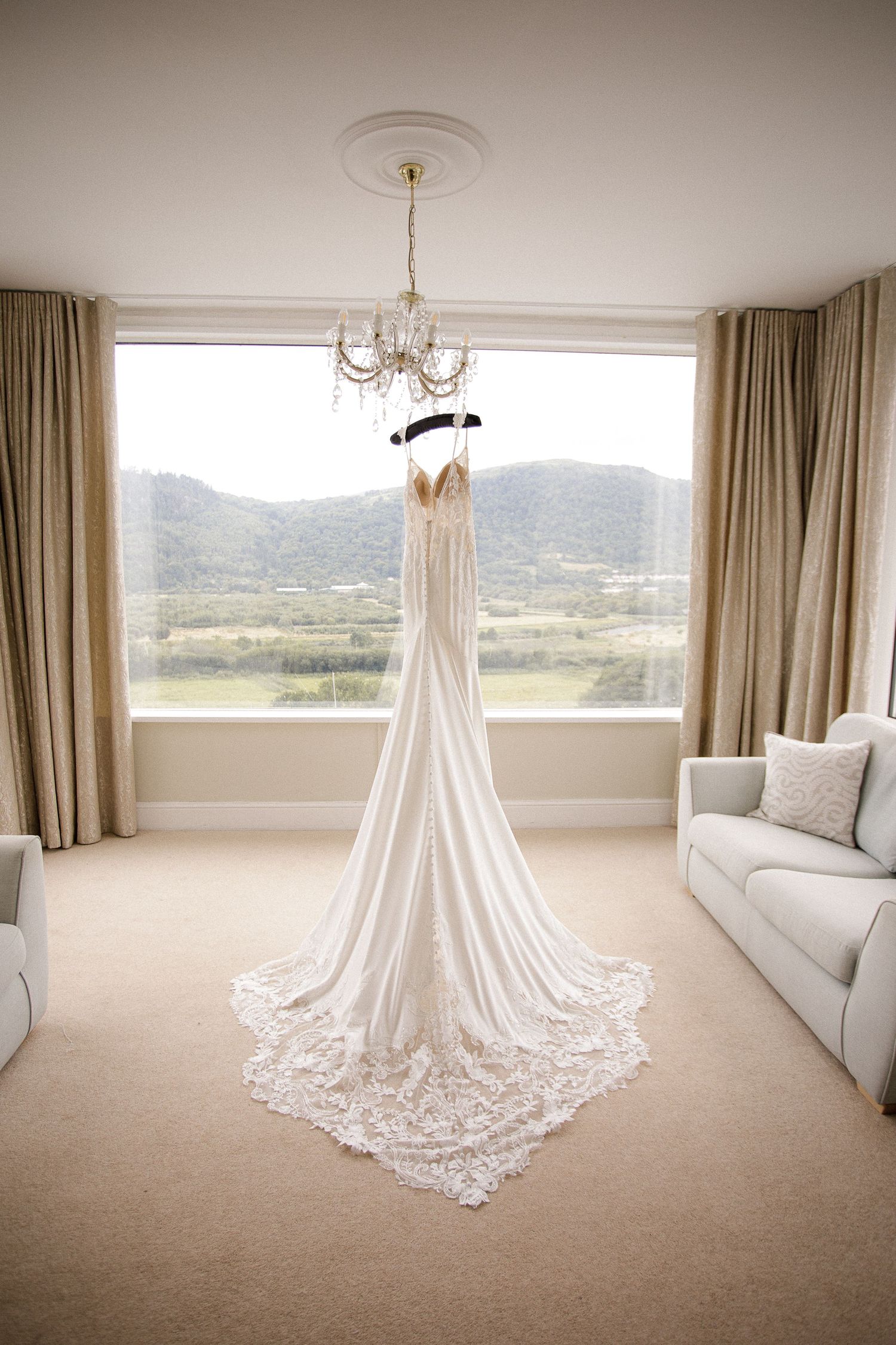A white lace wedding dress displayed in a bright room with mountain views through large windows.