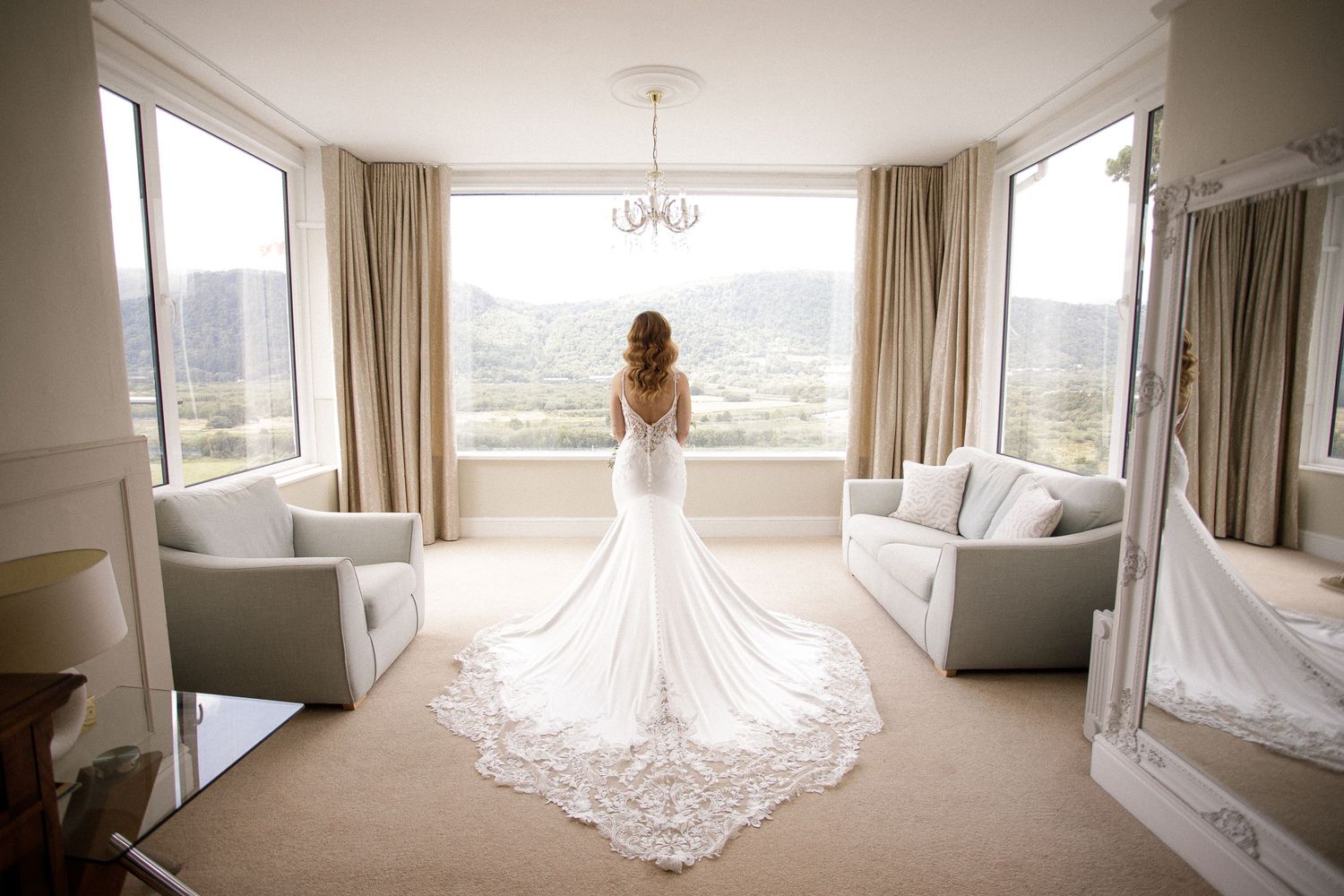Elegant bridal gown with flowing train displayed in a spacious, light-filled room with panoramic windows.