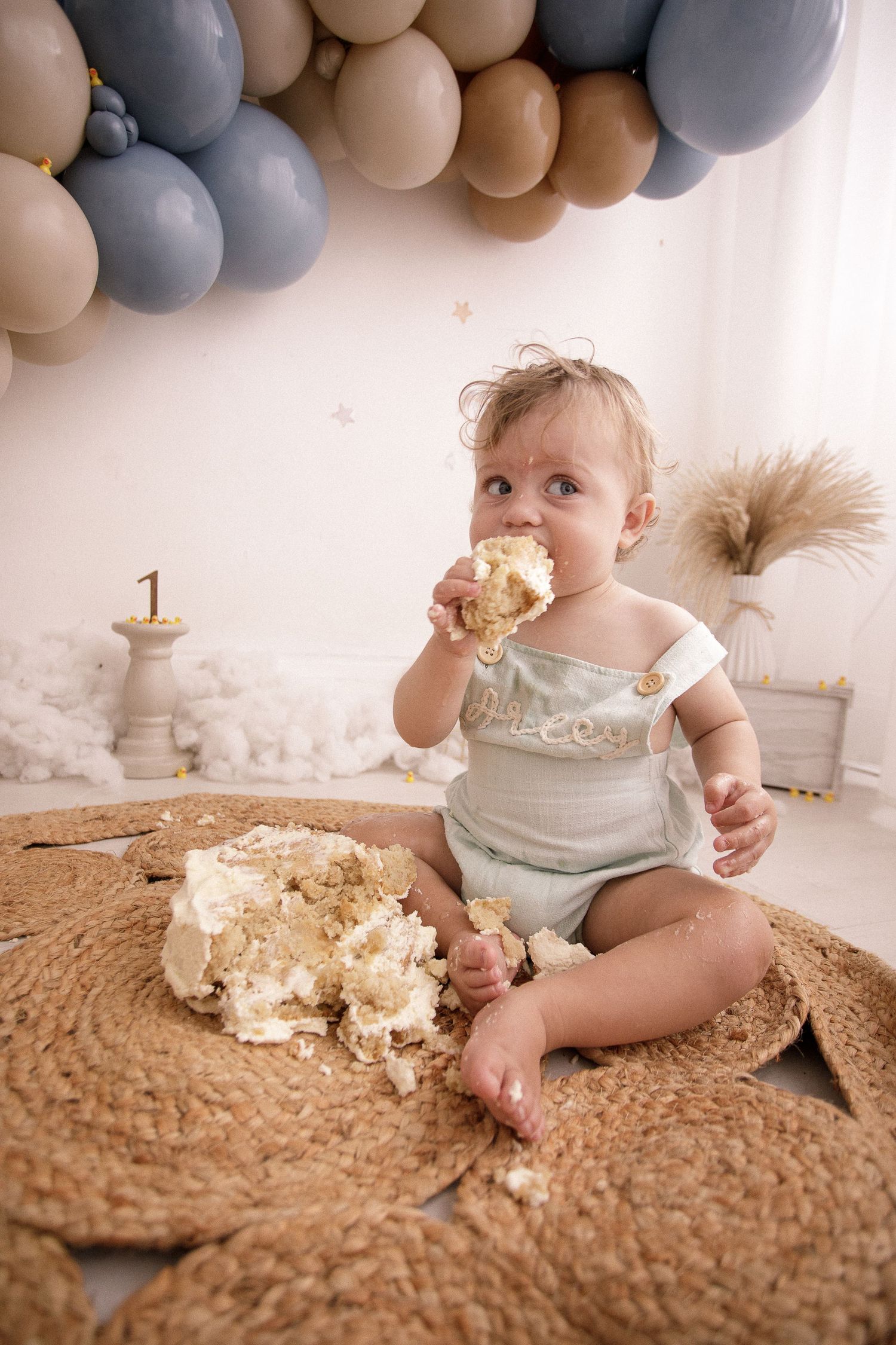 Baby enjoying cake smash photo session with grey and tan balloon decorations.