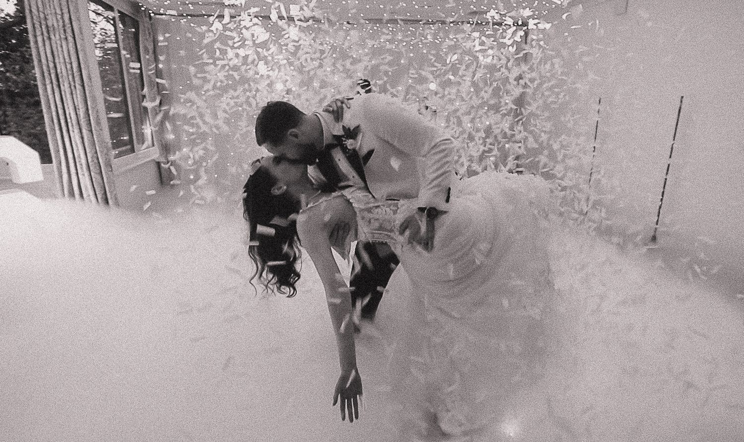 Black and white photo of winter wedding guests throwing confetti in celebration.