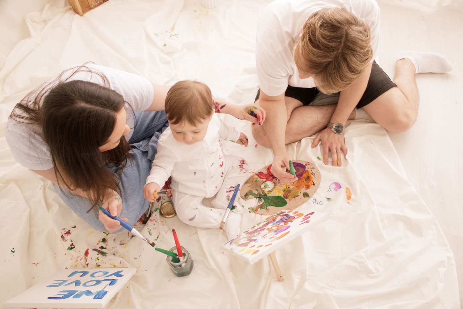 Creative art session with colorful paint and paper on floor.