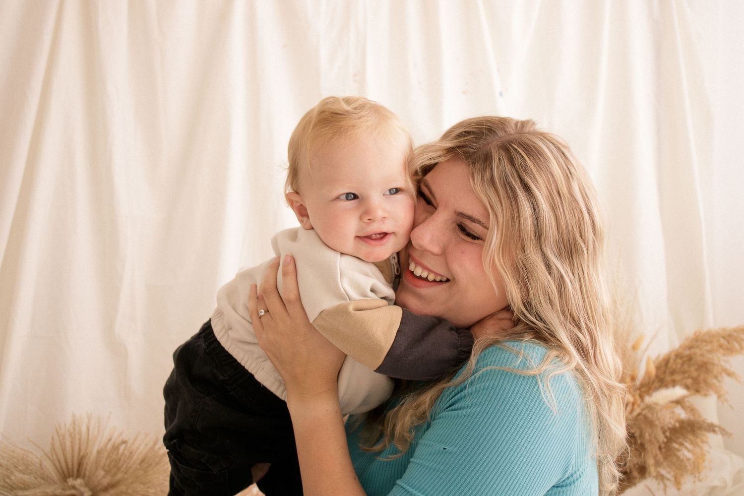 Sweet moment of parent and baby sharing affection against light curtain backdrop.