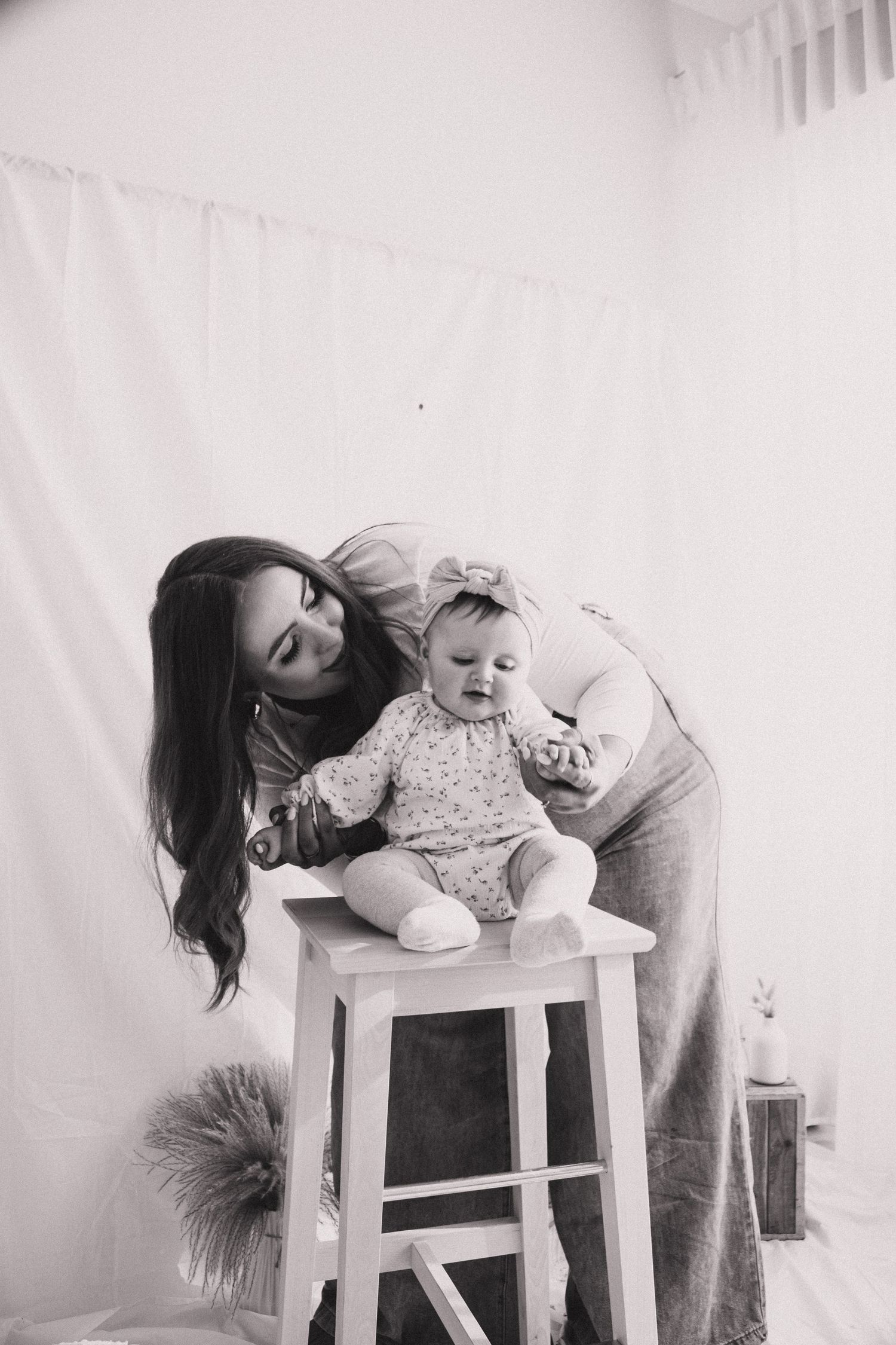 A series of black and white photos showing a baby sitting on a white chair while someone interacts with them.