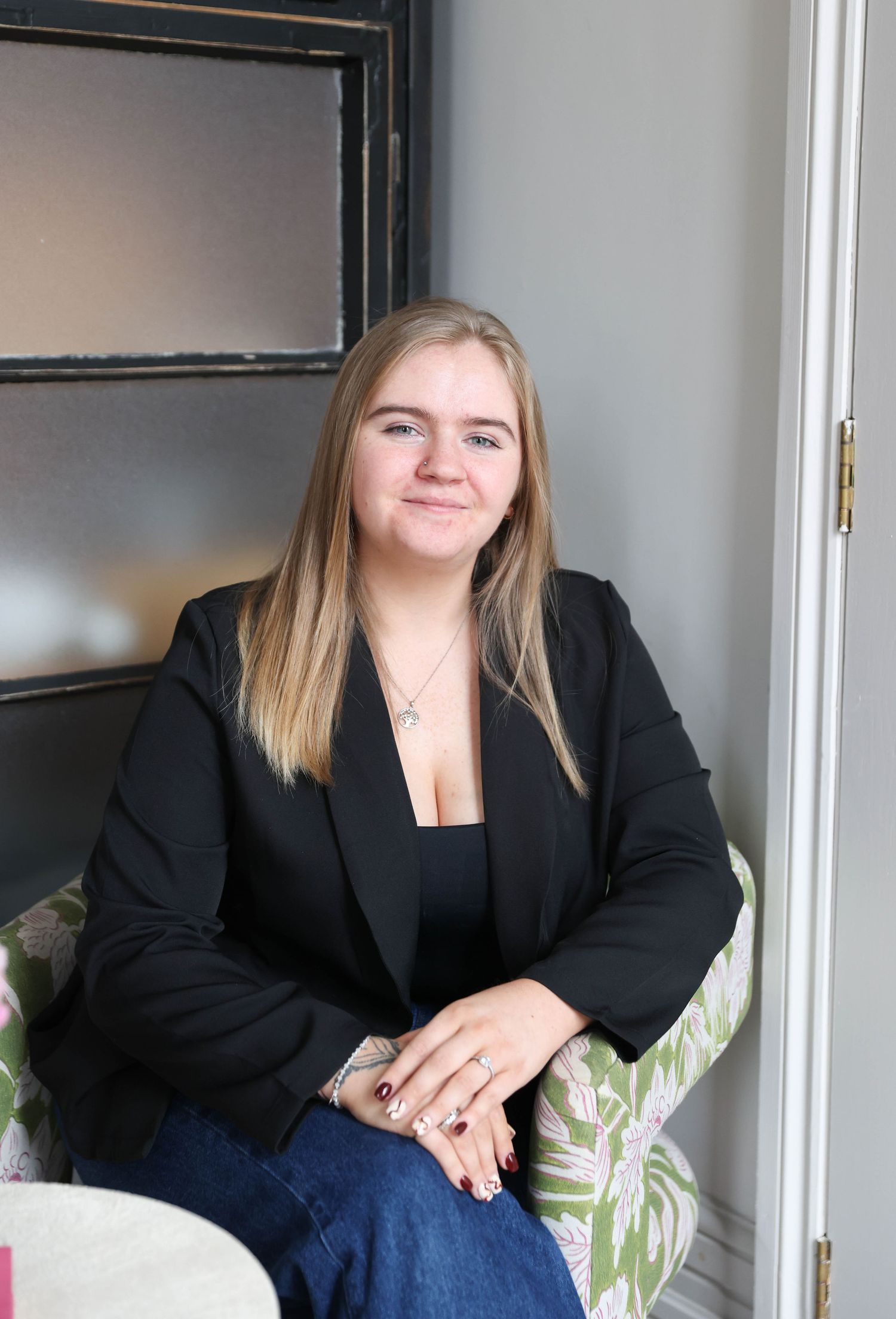 Casual professional portraits of person in black blazer and jeans seated in stylish setting.