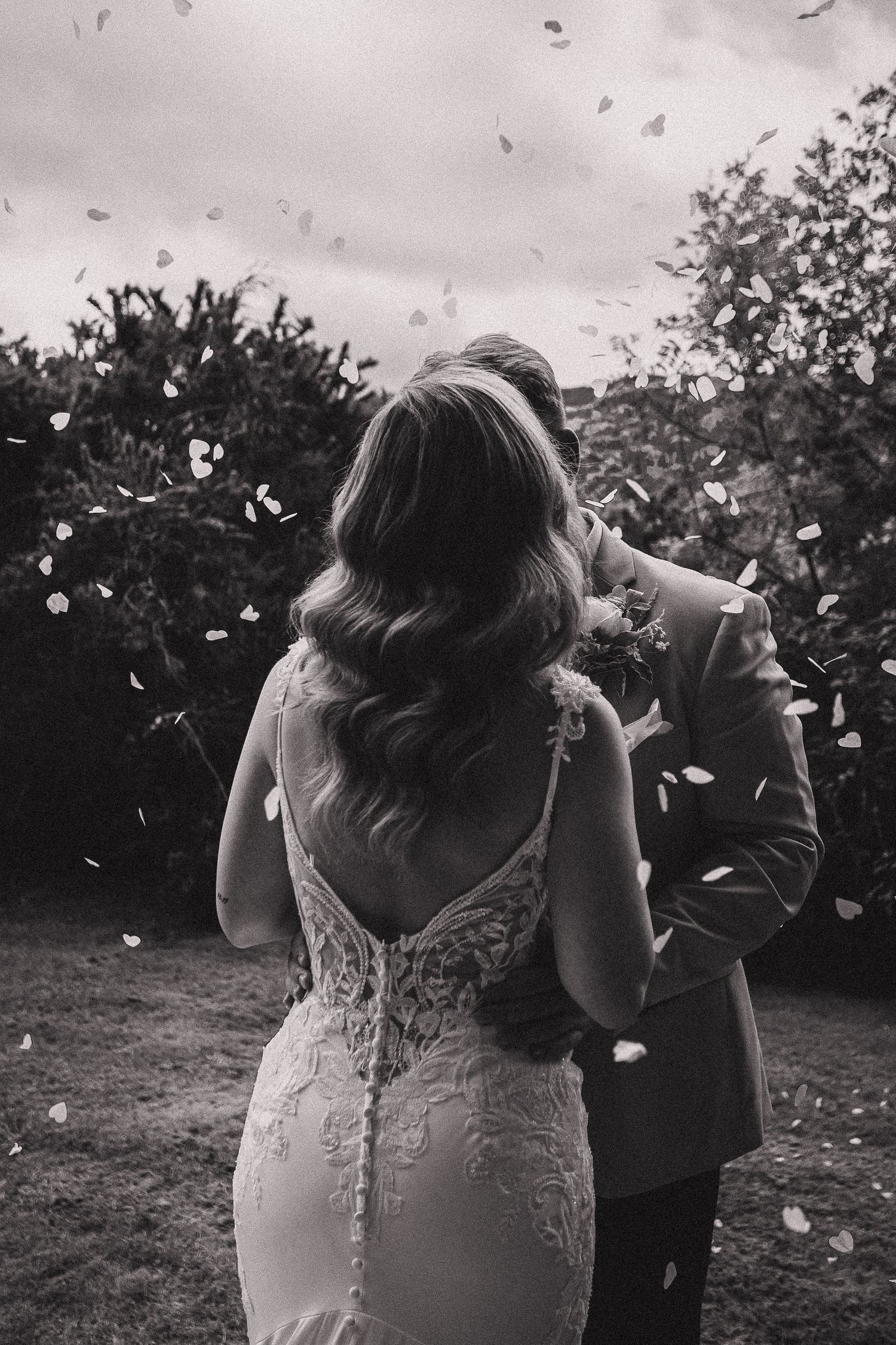 Confetti moment at outdoor wedding celebration captured in black and white.