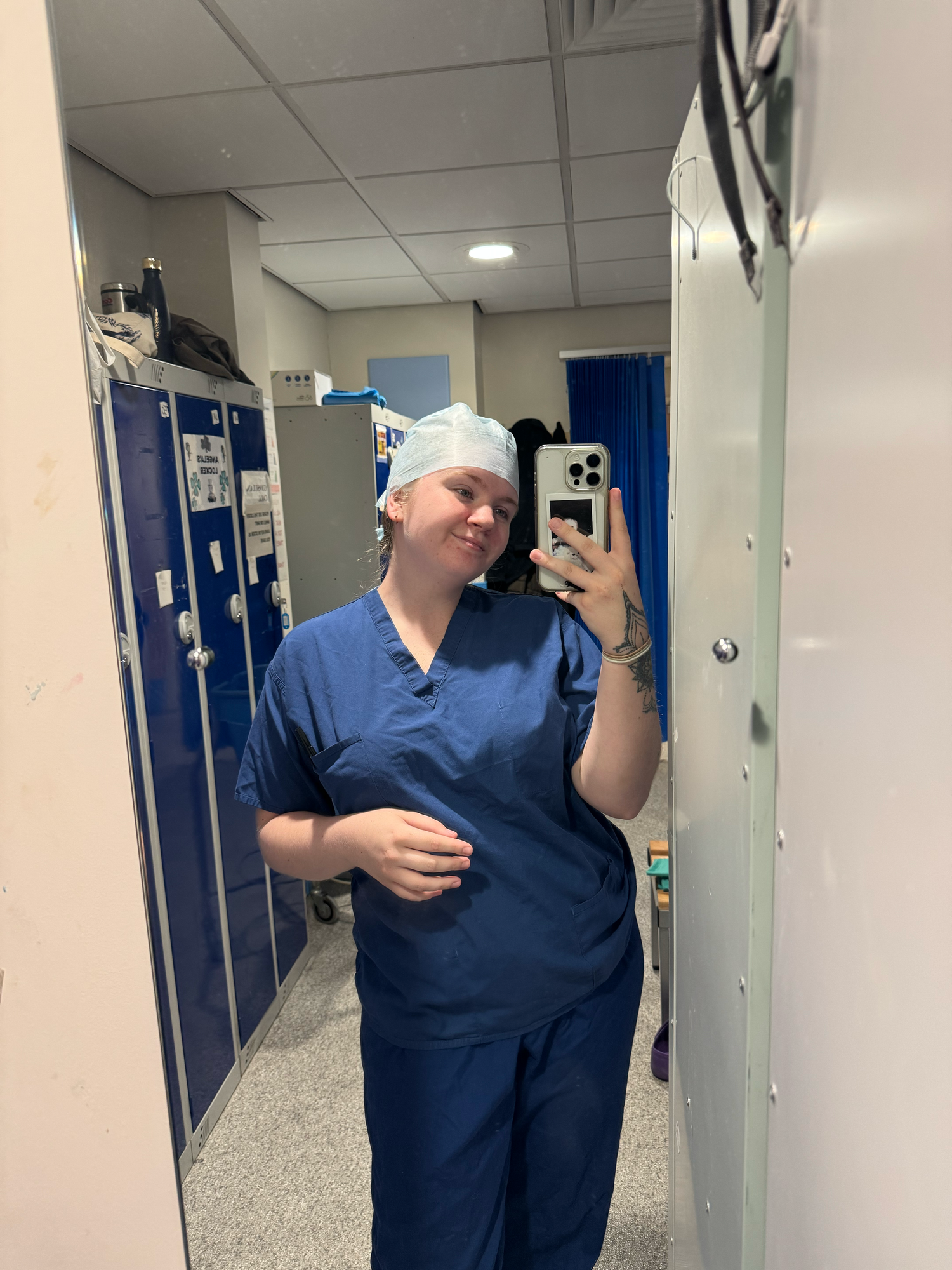 Healthcare worker in blue scrubs taking selfies in a hospital hallway.