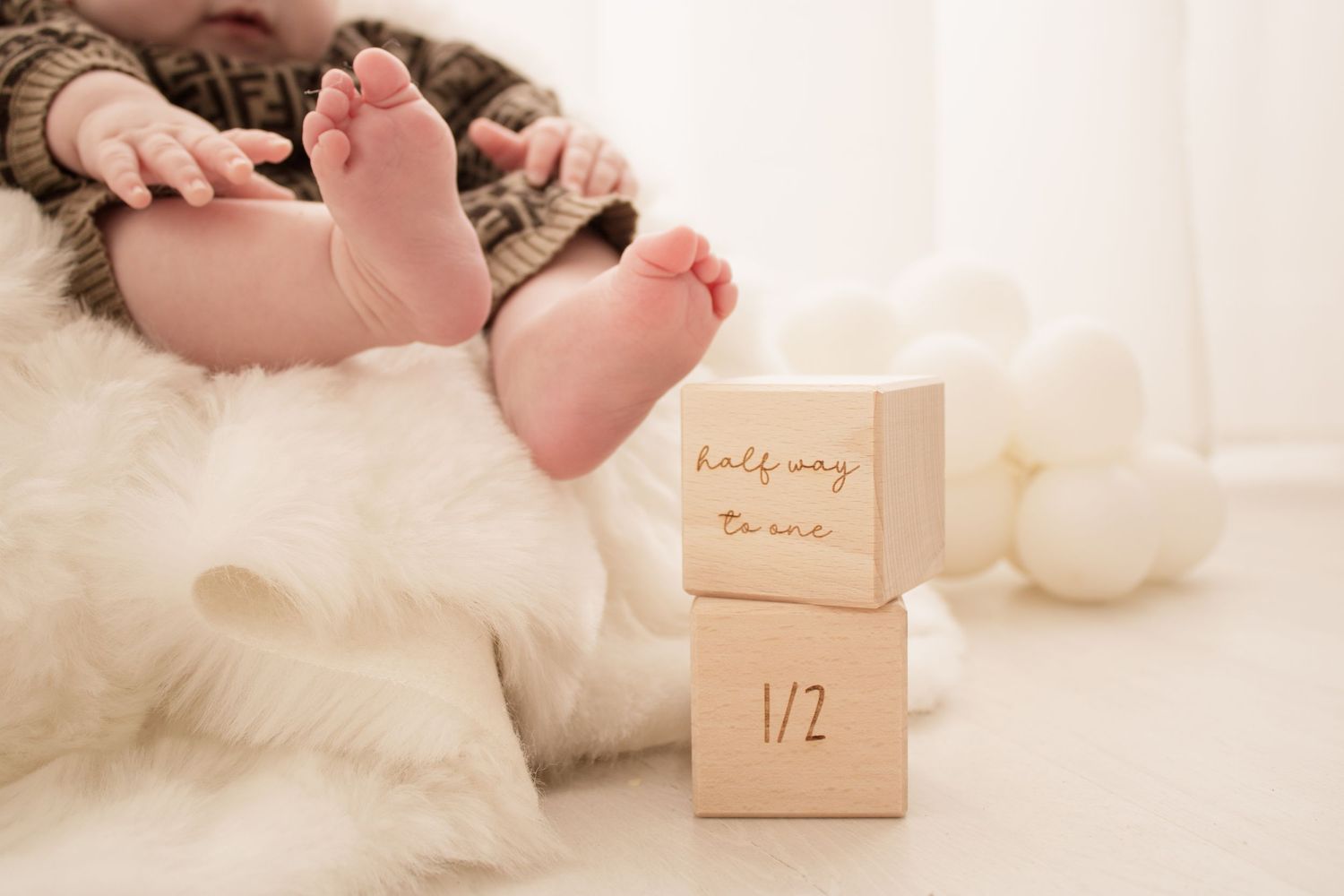 Tiny baby feet next to wooden milestone blocks on white furry backdrop.
