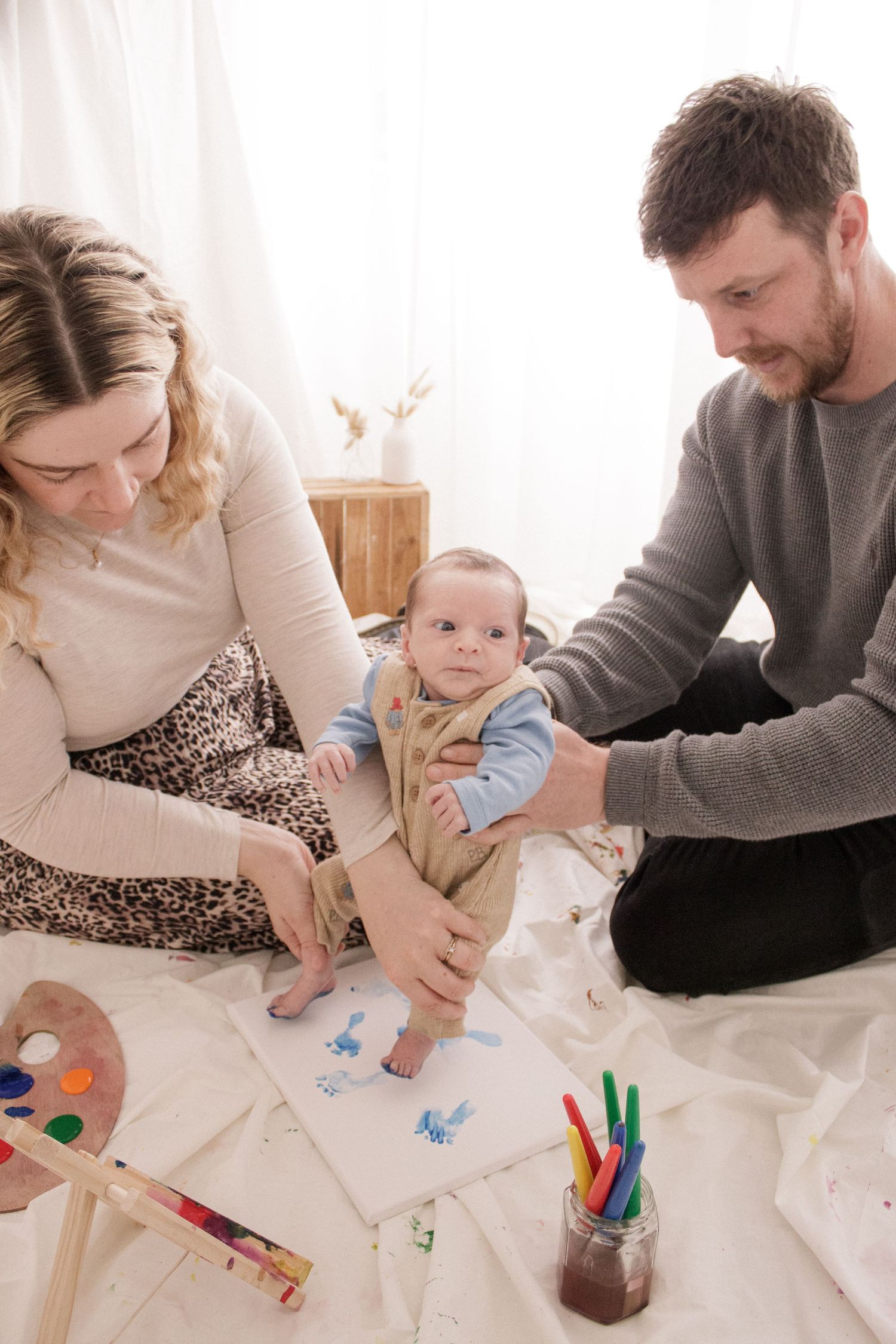 Family sits together on floor drawing and coloring with art supplies on white paper spread across carpet.