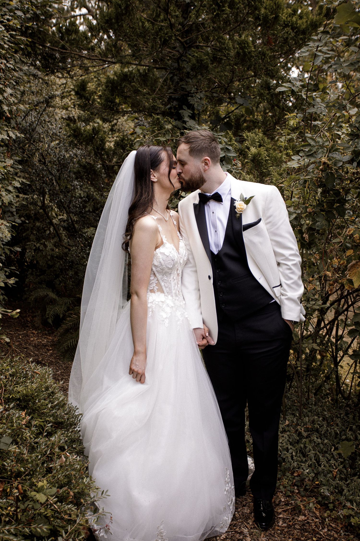 A romantic wedding photoshoot in a wooded outdoor setting with a couple in white and black attire.