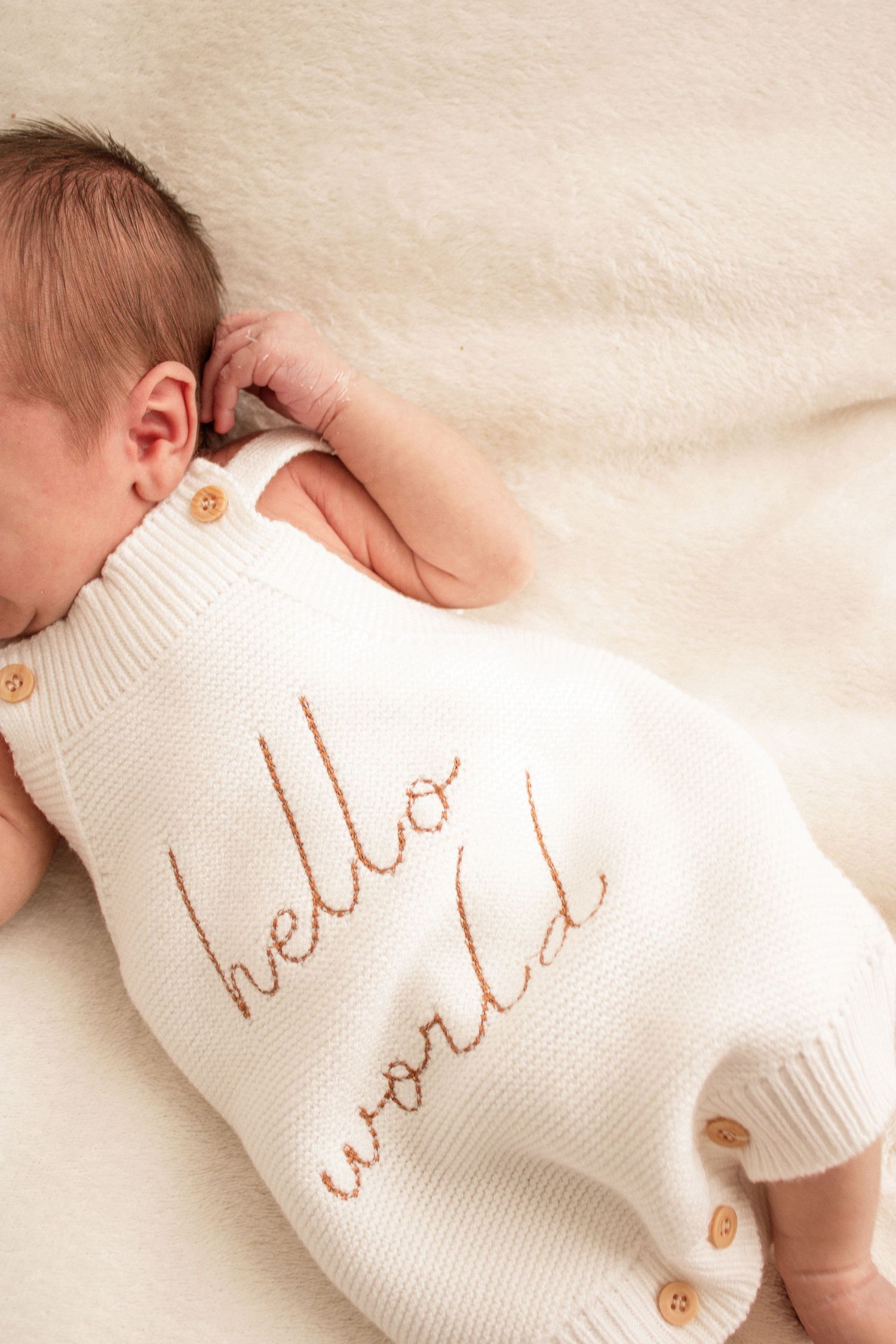 Close-up series showing white baby clothing with delicate text embroidery and wooden buttons.