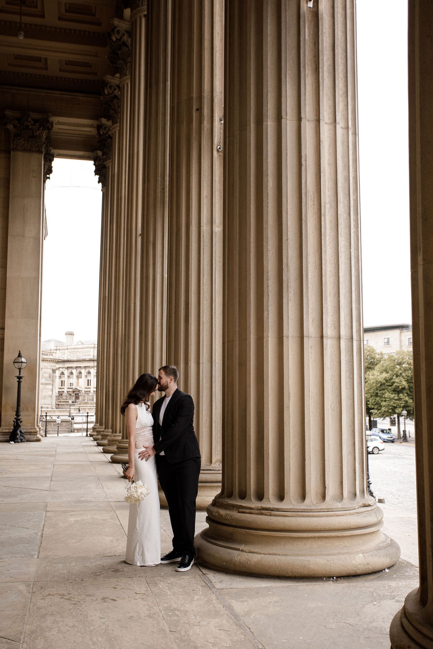 Wedding photography session among classical stone columns of a grand building.
