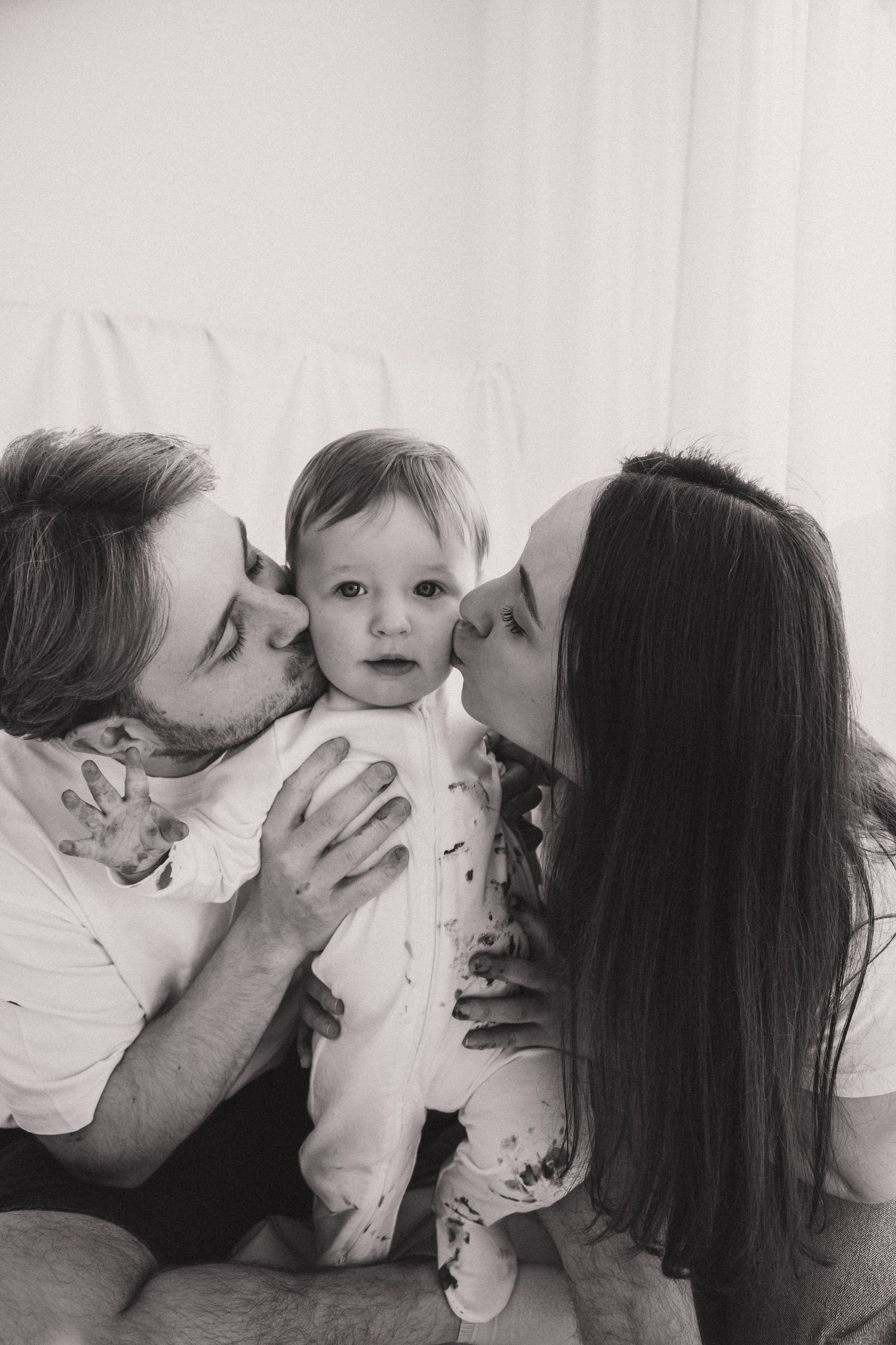 A series of black and white photos showing tender family moments with a baby being kissed by parents.