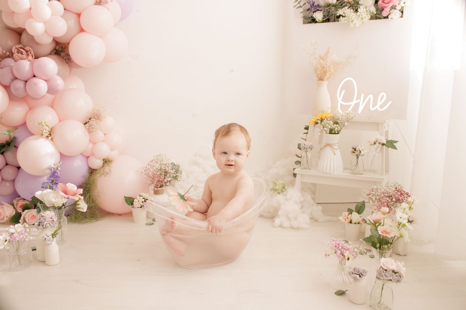 First birthday setup with pink and purple balloon arch and floral decorations.