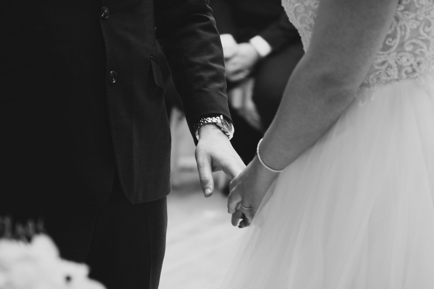 Black and white photo capturing hands during an intimate wedding ceremony moment.