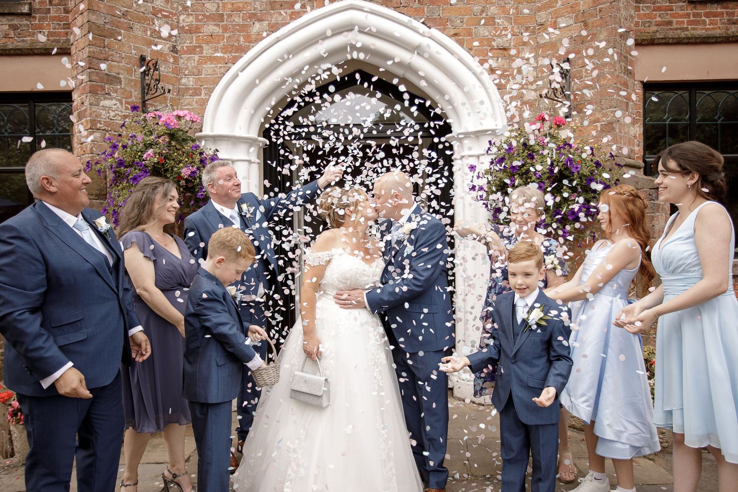 Wedding party celebrating with confetti outside a brick church with arched doorway.