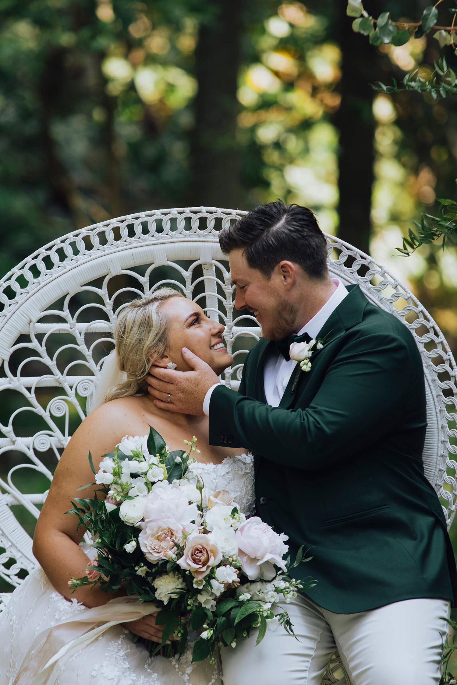 Groom sitting on chair arm with hand on bride's chin looking at each other in Palm Beach - Zara King Photography, Sydney Australia
