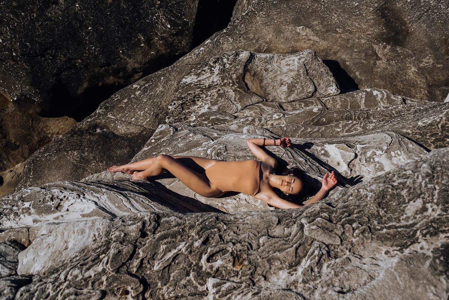 Birds eye view of girl in swimsuit lying on rocks during modelling photo shoot at Clovelly beach - Zara King Photography, Sydney Australia