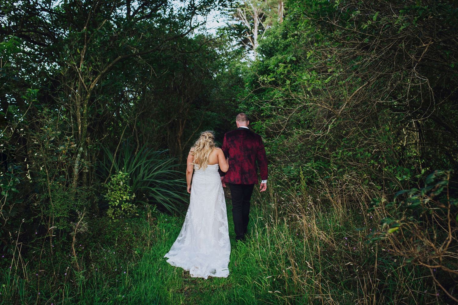 Bride and groom holding hands walking away down an overgrown path in Dunedin, NZ - Zara King Photography,