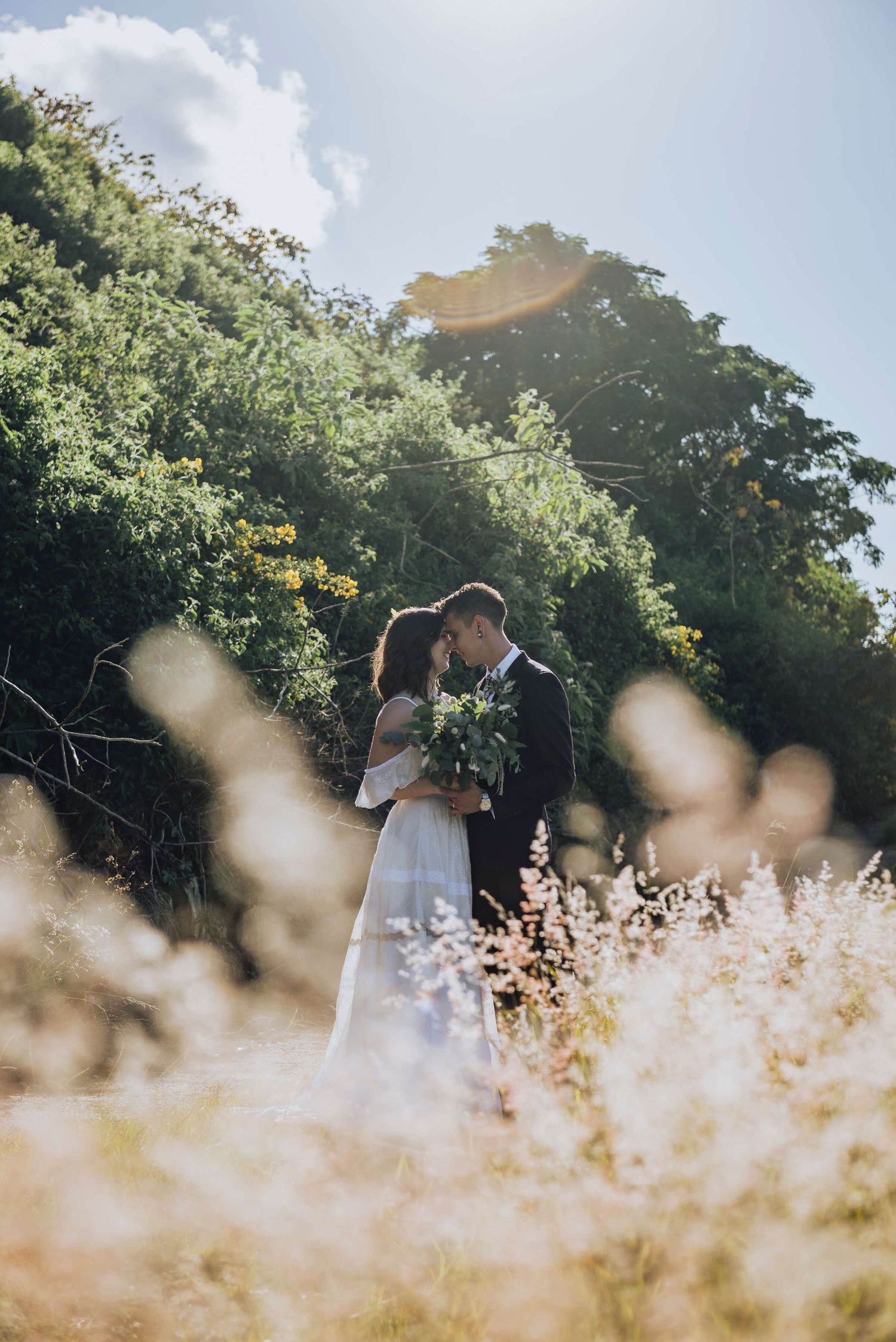 Bride and groom cuddling surrounded by wild grass in Wahroonga - Zara King Photography, Sydney Australia