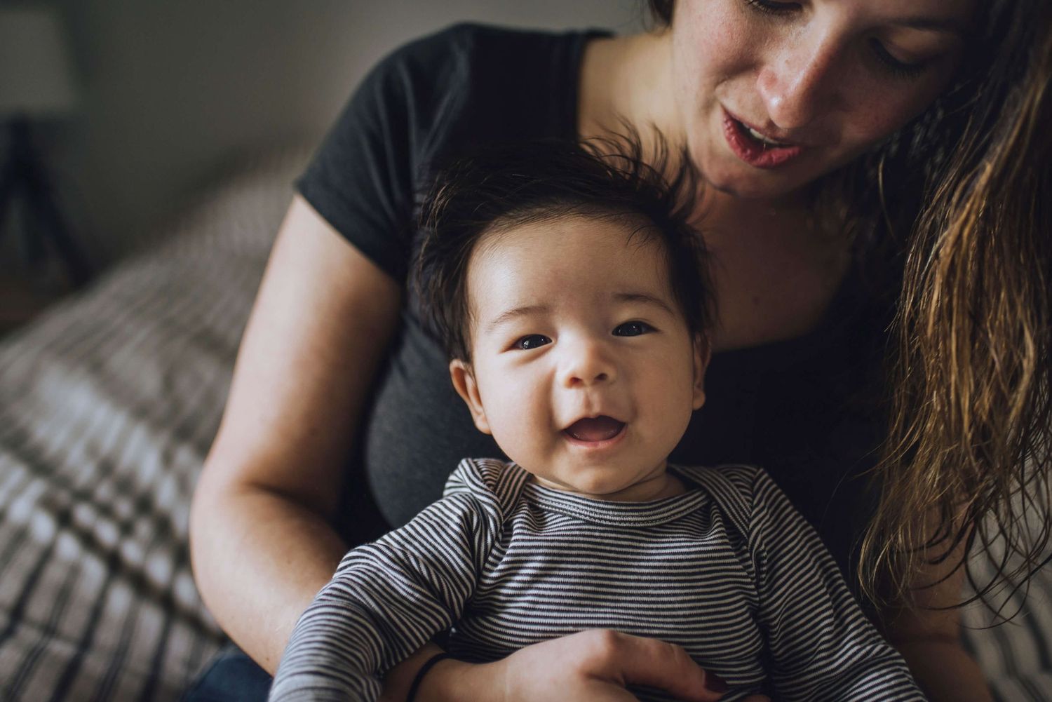 Candid portrait of baby smiling in mother's lap during in-home session - Zara King Photography, Sydney Australia