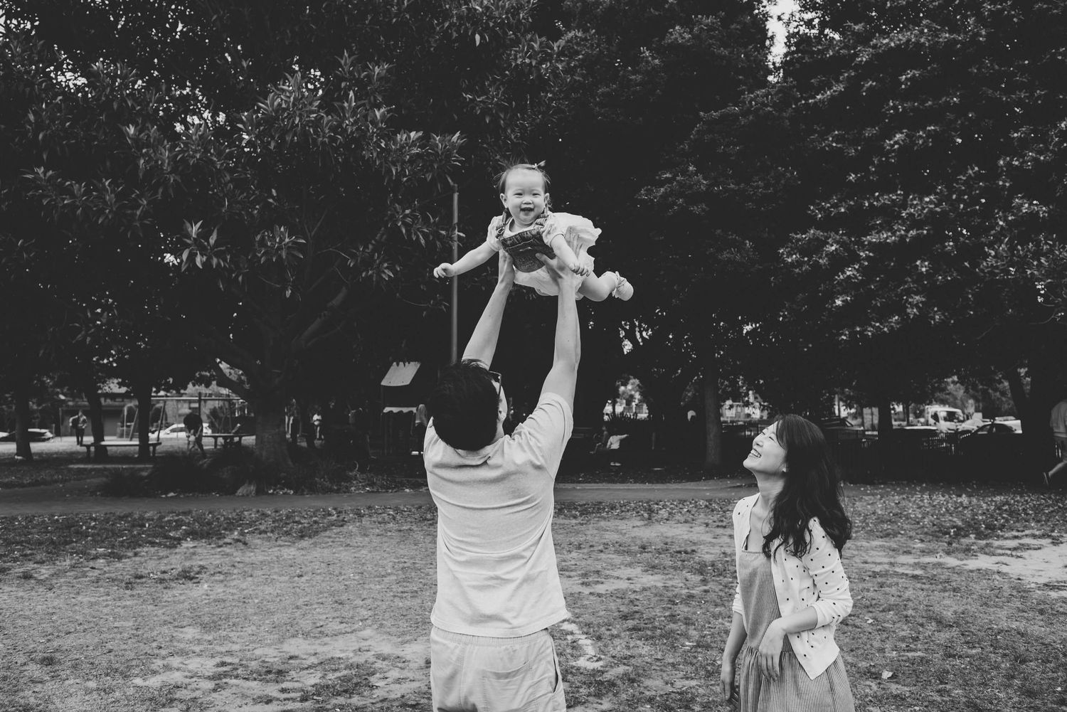 Dad throwing baby daughter in the air while mum watches and laughs during outdoor family session - Zara King Photography, Sydney Australia