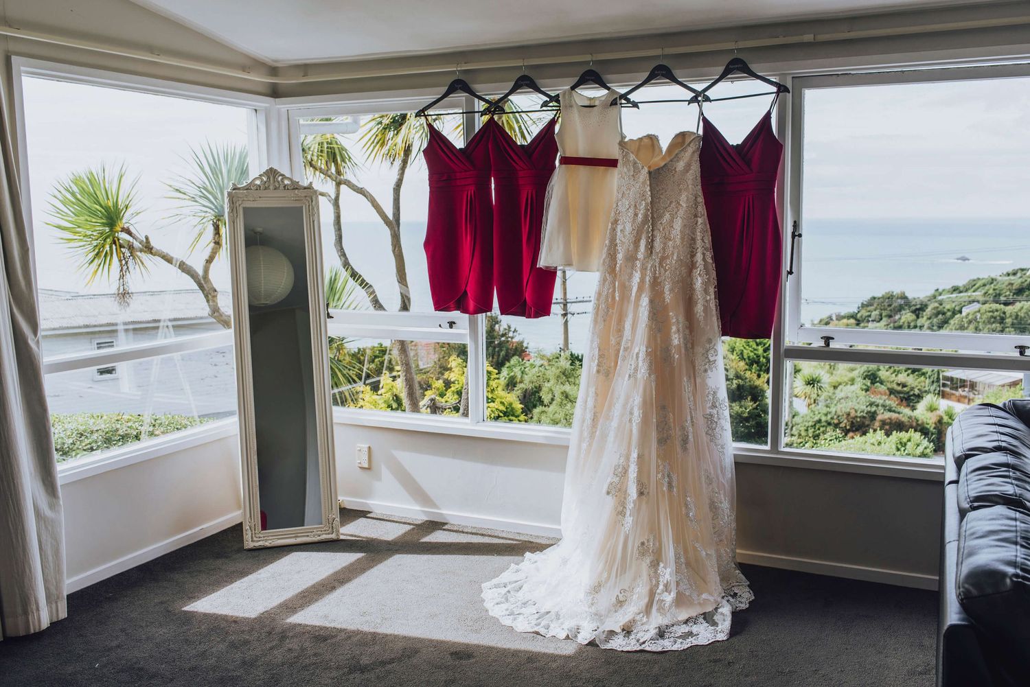 Bride and bridesmaid dresses all lined up in the window overlooking the ocean in Dunedin, NZ - Zara King Photography
