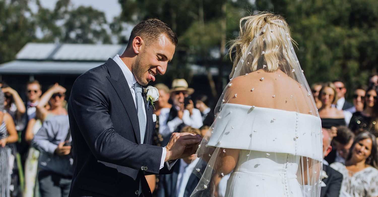 Groom sticks tongue out while putting ring on bride's finger during their ceremony in Kangaroo Valley - Zara King Photography, Sydney