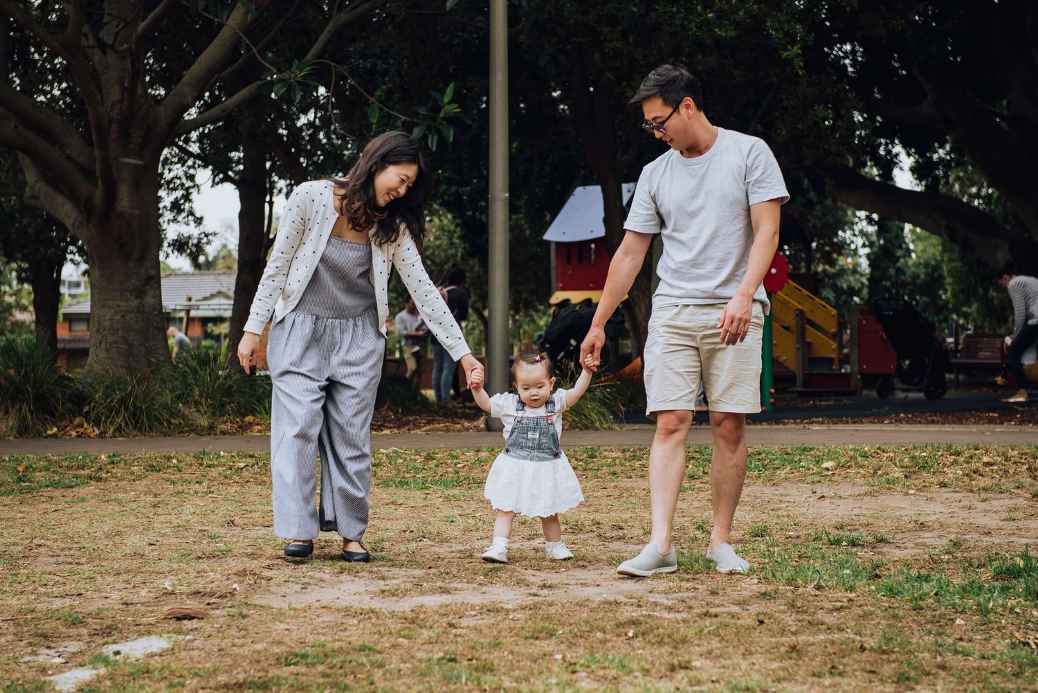 Parents helping baby daughter walk during outdoor family session in Rosebery - Zara King Photography, Sydney Australia