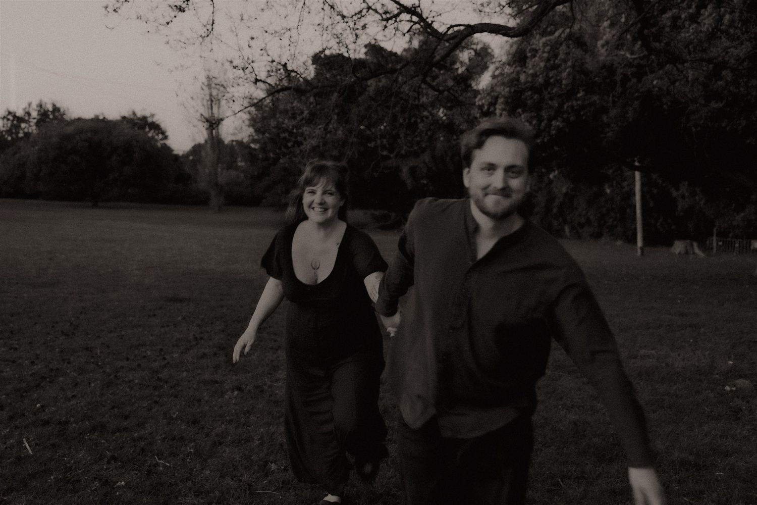 Zara King and fiancé running, he's leading her through a field towards the photographer