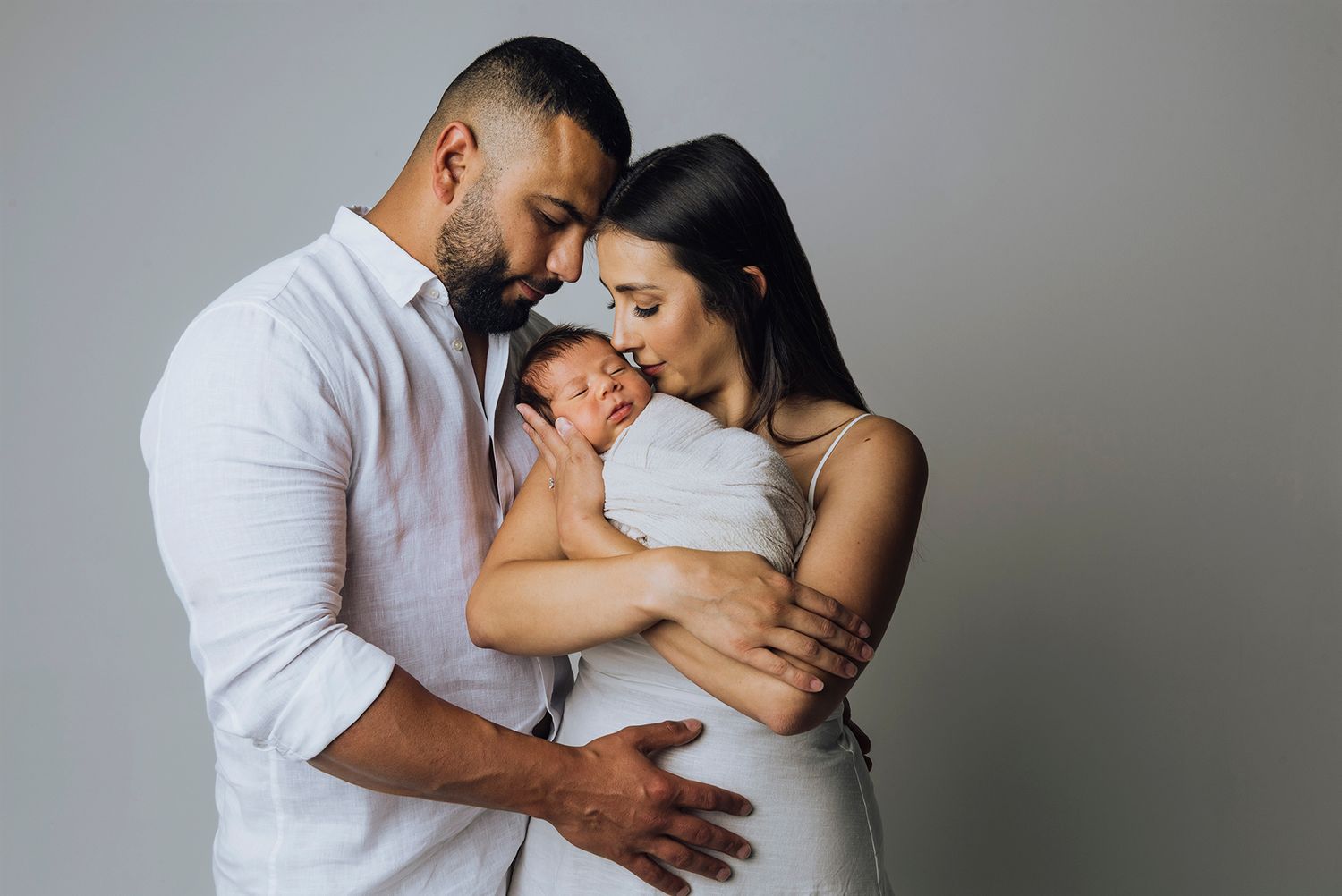Young couple cuddling with their foreheads touching while mum holds newborn baby - Zara King Photography, Sydney Australia