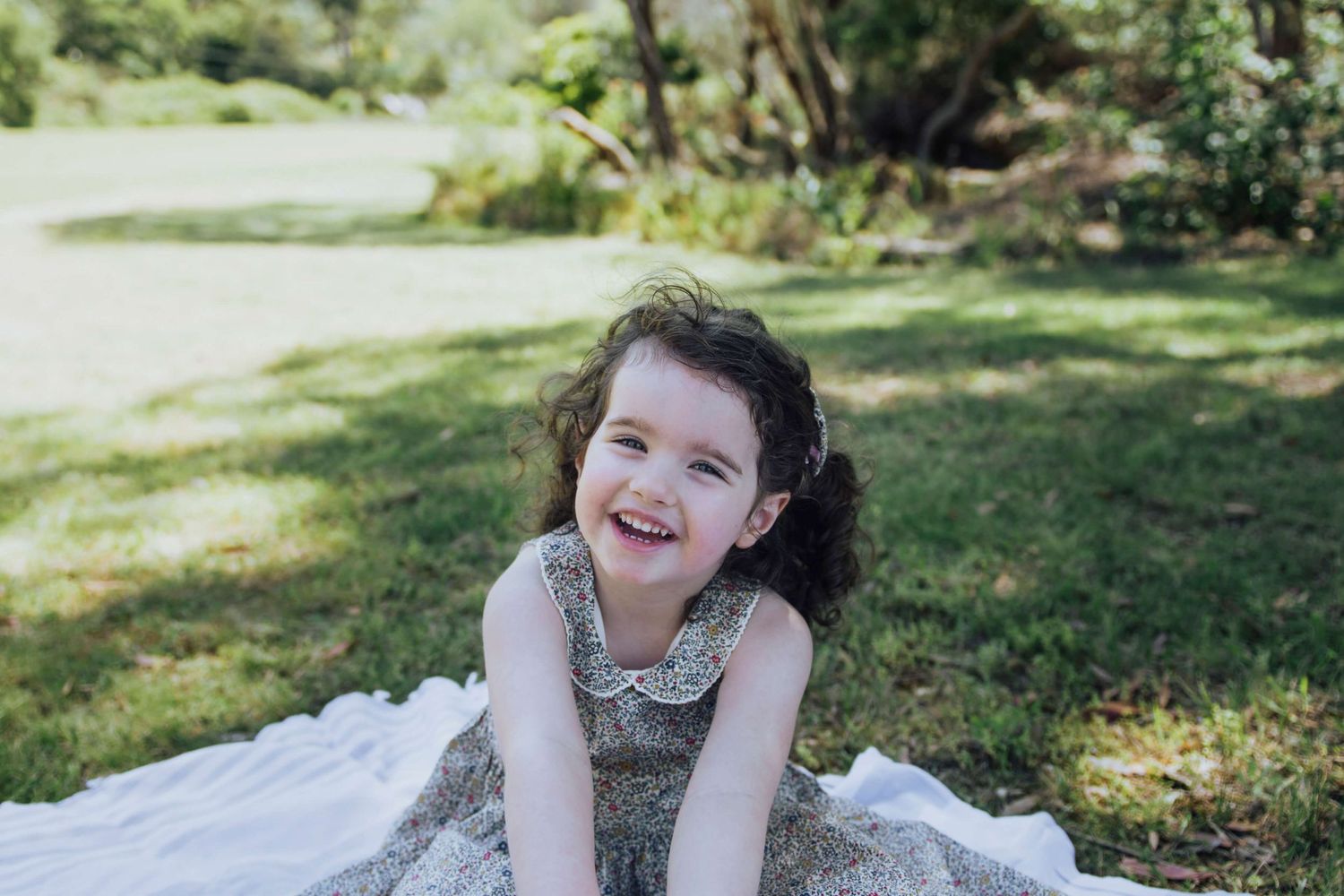 Little girl smiling at camera sitting on a picnic blanket in her backyard during at-home session - Zara King Photography, Sydney Australia