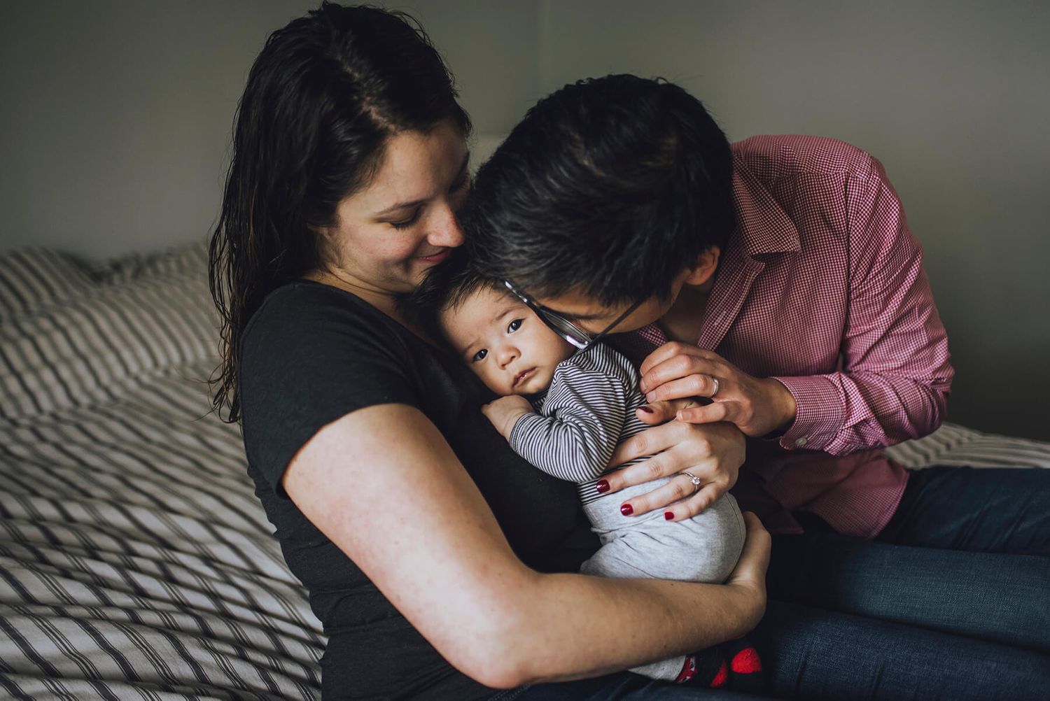 Candid portrait of mum holding newborn baby boy while dad kisses his cheek during in-home session  - Zara King Photography, Sydney Australia