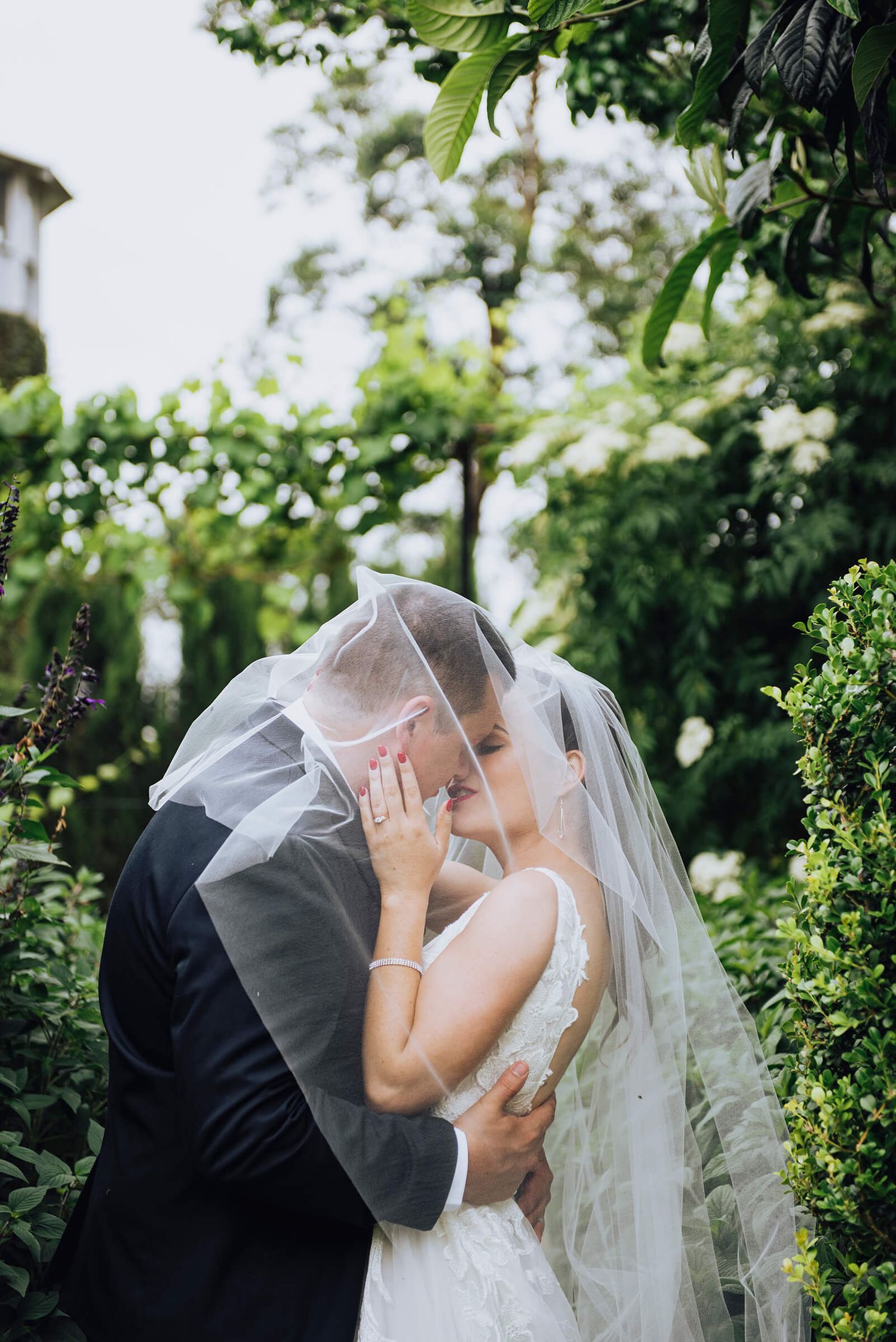 Bride and groom kiss under bride's vail in gardens at The Merribee in Nowra - Zara King Photography, Sydney Australia
