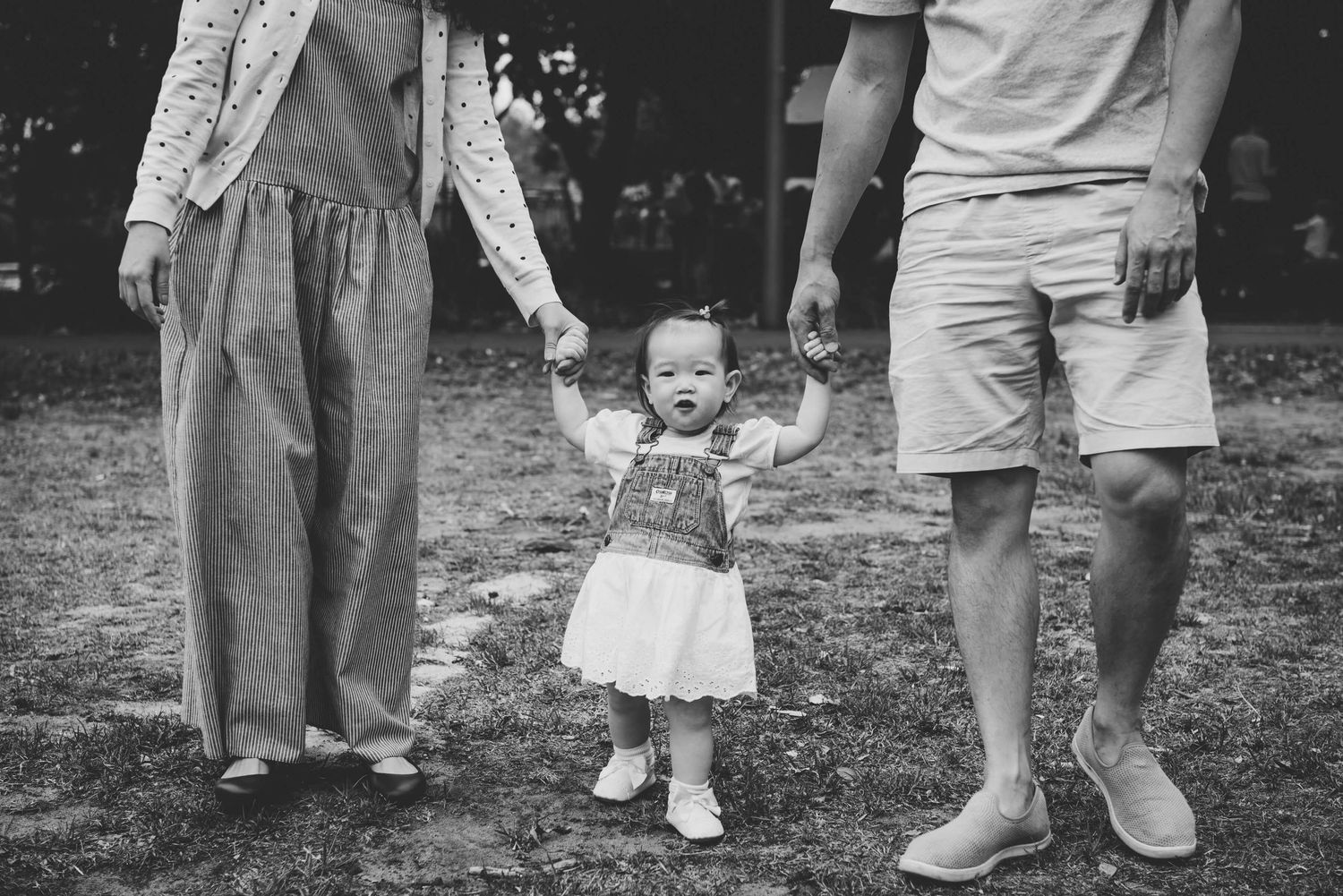 Close up of baby girl walking while holding her parent's hands during outdoor family session - Zara King Photography, Sydney Australia