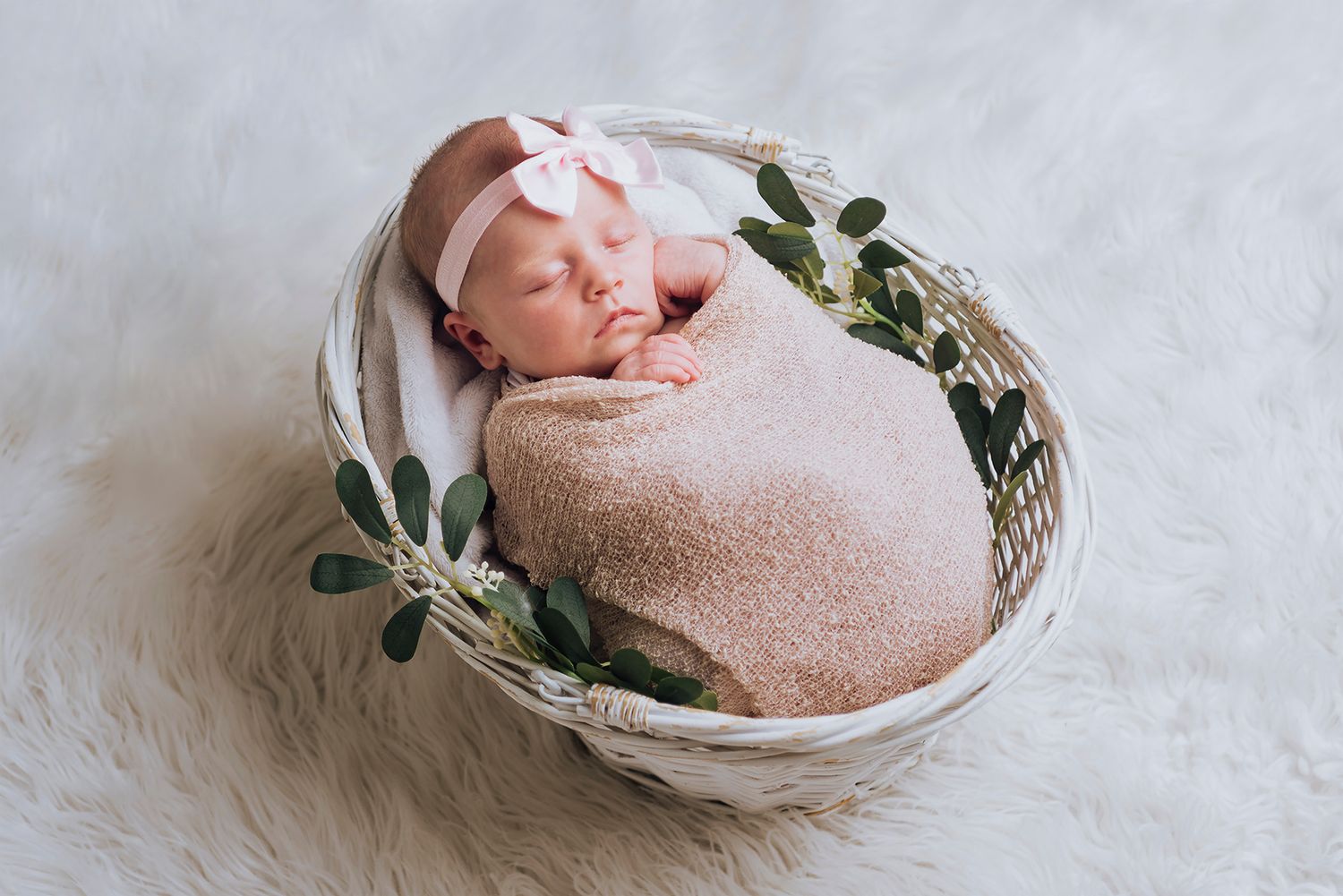 Newborn baby girl wearing a pink bow wrapped in a swaddle in a basket - Zara King Photography, Sydney Australia