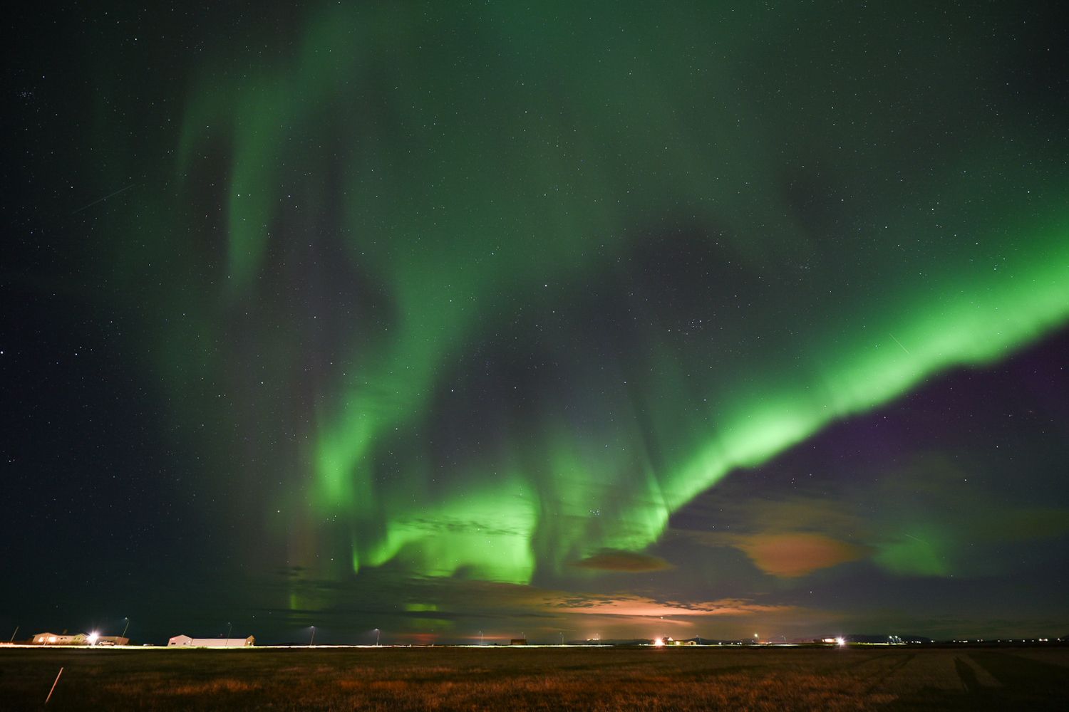 Vibrant green aurora borealis northern lights dancing across the night sky over a dark landscape in Iceland.