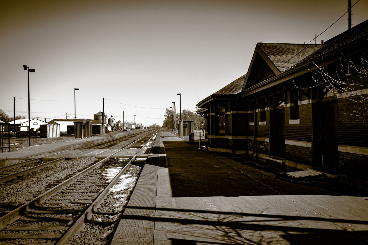 Vintage sepia photo of a quiet train station platform at Osceola, Iowa with railroad tracks and a historic depot building.