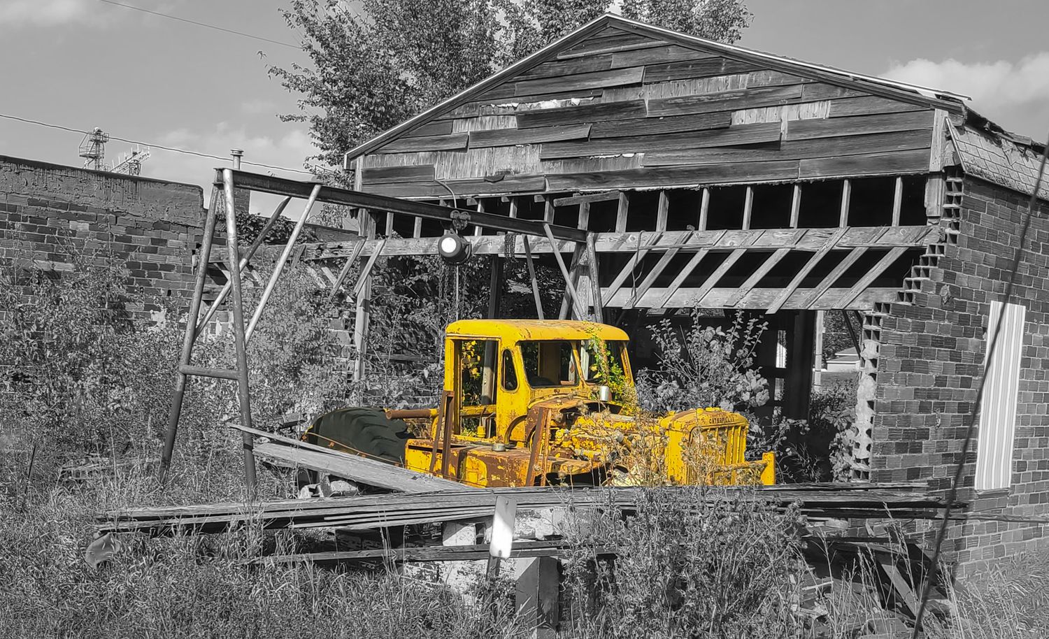 Vintage yellow bulldozer parked inside a deteriorating wooden barn structure in black and white landscape.