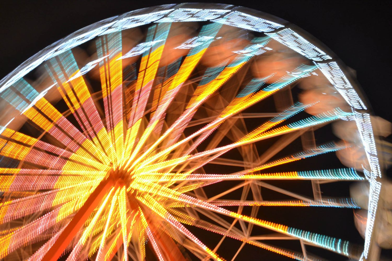Colorful illuminated Ferris wheel spinning at night with vibrant orange, blue, and yellow lights at the Iowa State Fair midway.