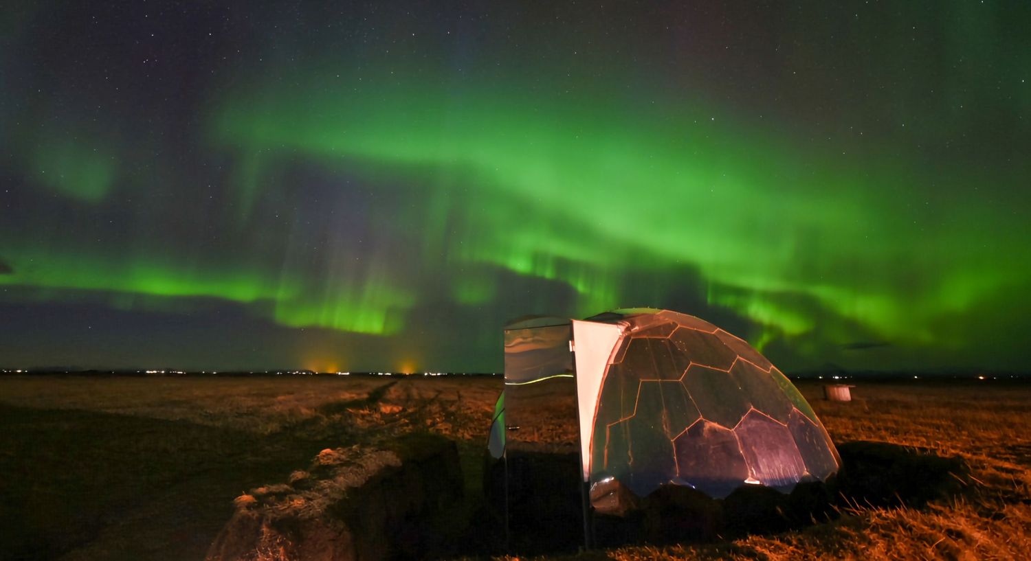 Vibrant green northern lights aurora borealis illuminating the night sky over a dome tent.