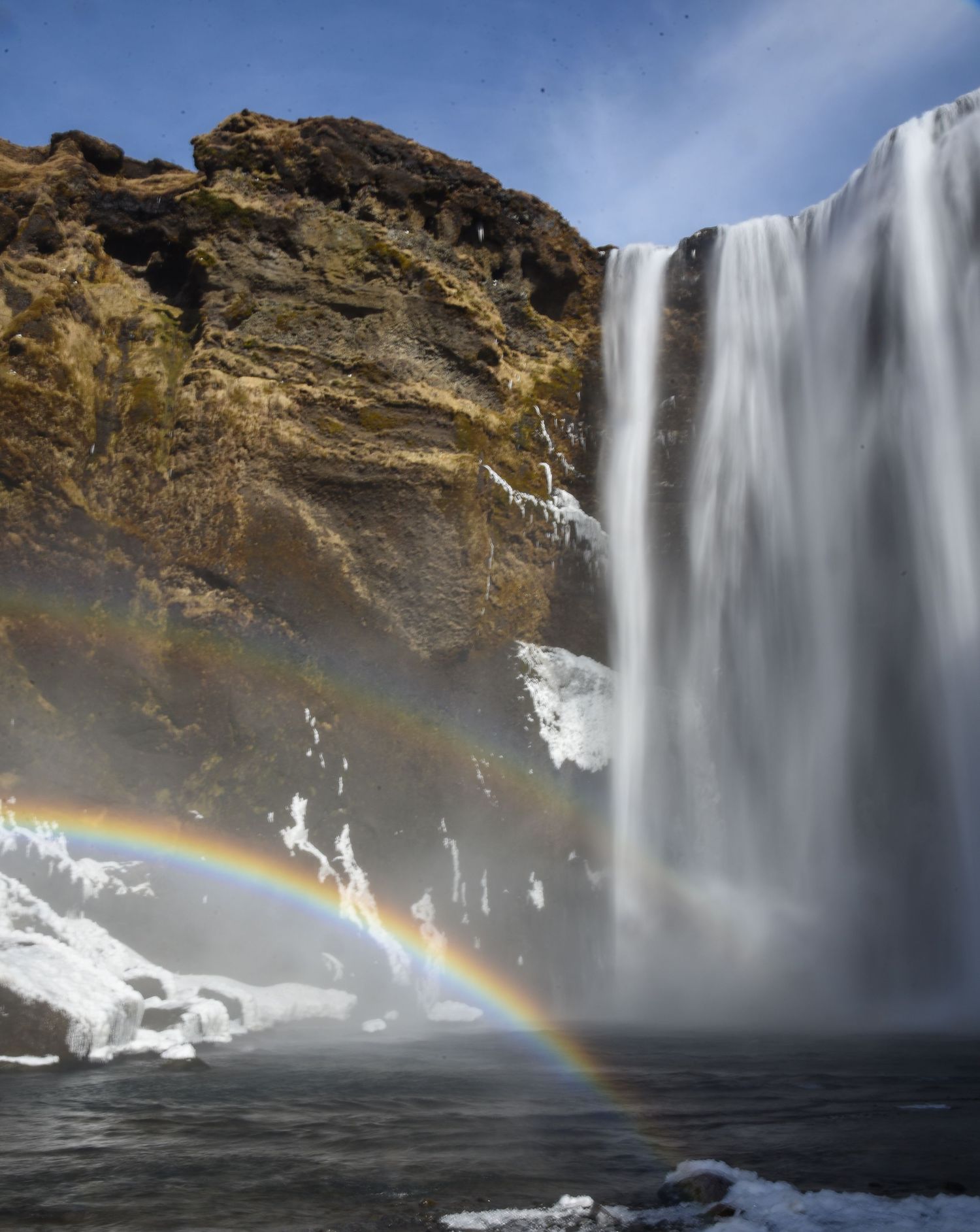 Skogafoss waterfall in Iceland cascading over rocky cliffs with a stunning rainbow visible in the mist.