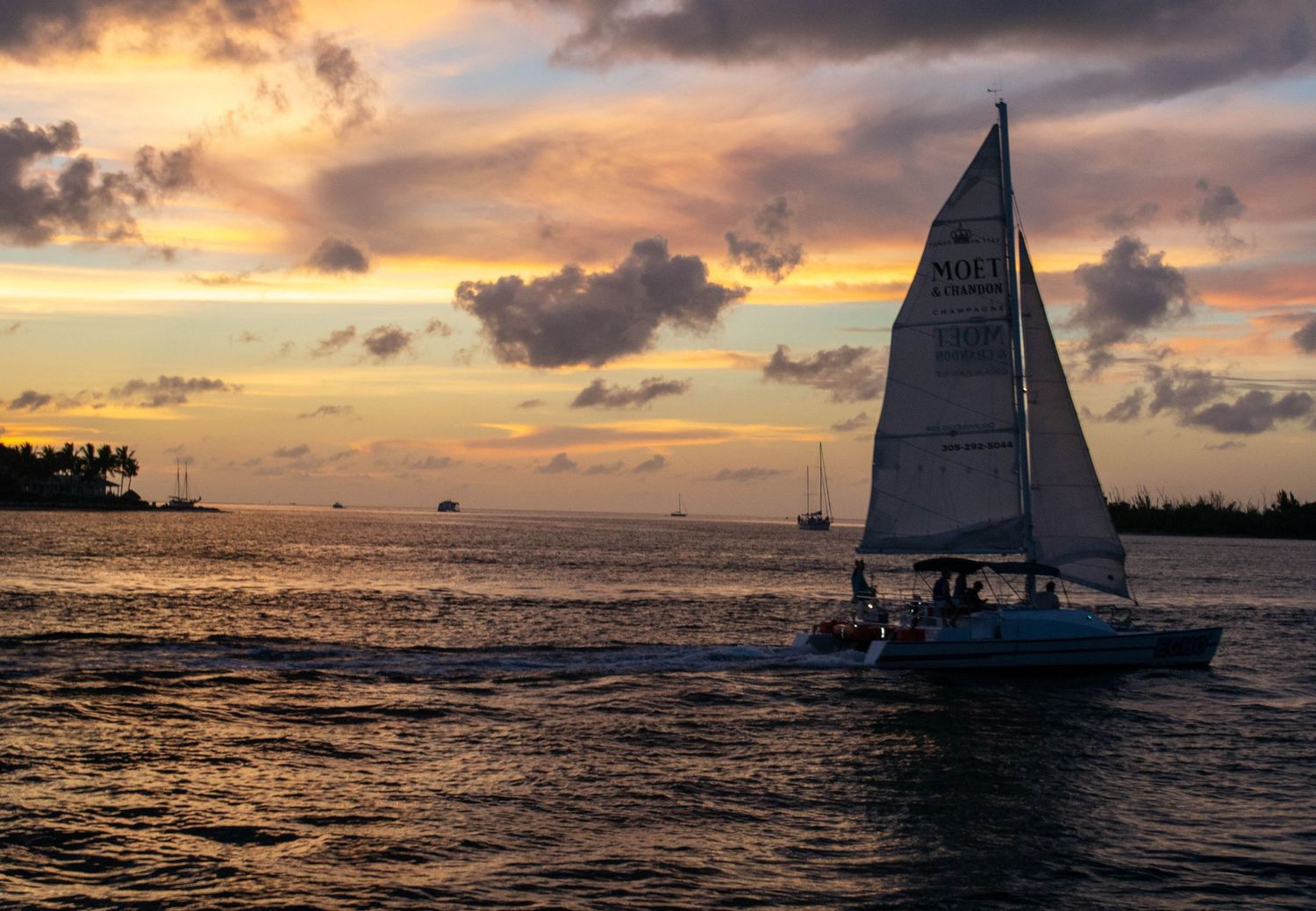 Sailboat silhouetted against a vibrant sunset at Key West, Florida with dramatic clouds over calm ocean waters.