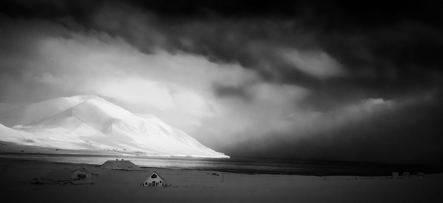 Dramatic black and white landscape of a snow-covered volcanic mountain under stormy skies in Iceland.