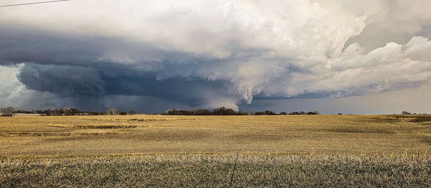 Massive supercell thunderstorm with rotating wall cloud forms over flat open farmland during daytime. F3 tornado near Keota, Iowa Mar-24