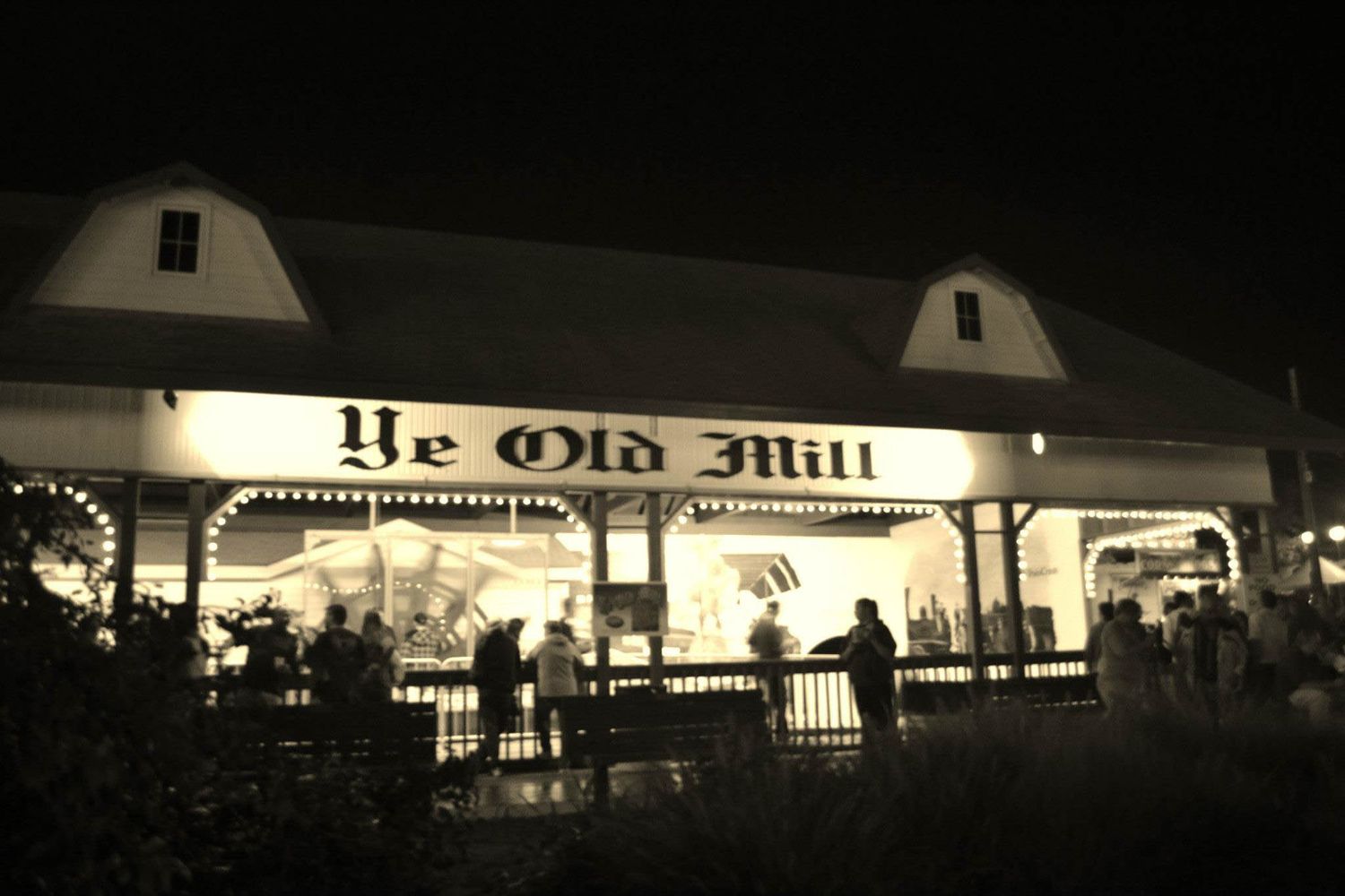 Ye Old Mill illuminated at night with visitors gathered outside the historic building.