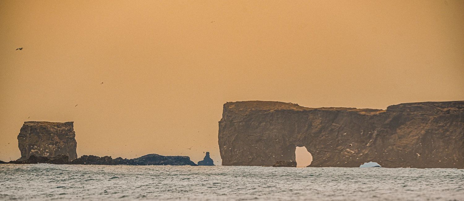 Golden sunset silhouettes dramatic coastal rock formations and a natural arch rising from the sea.