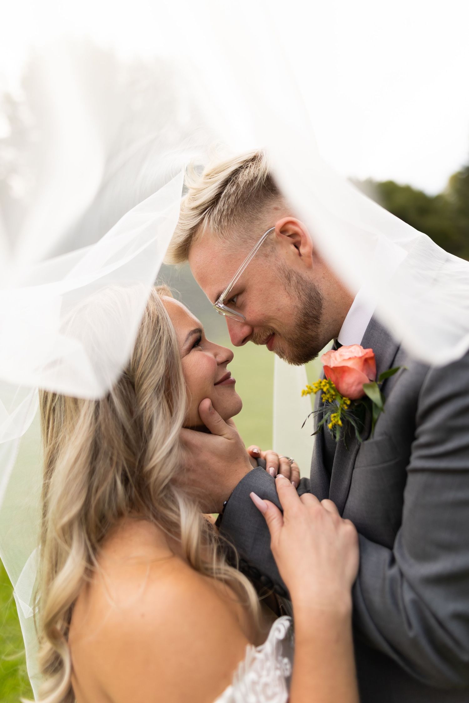 A romantic wedding portrait with flowing veil in soft natural lighting outdoors.