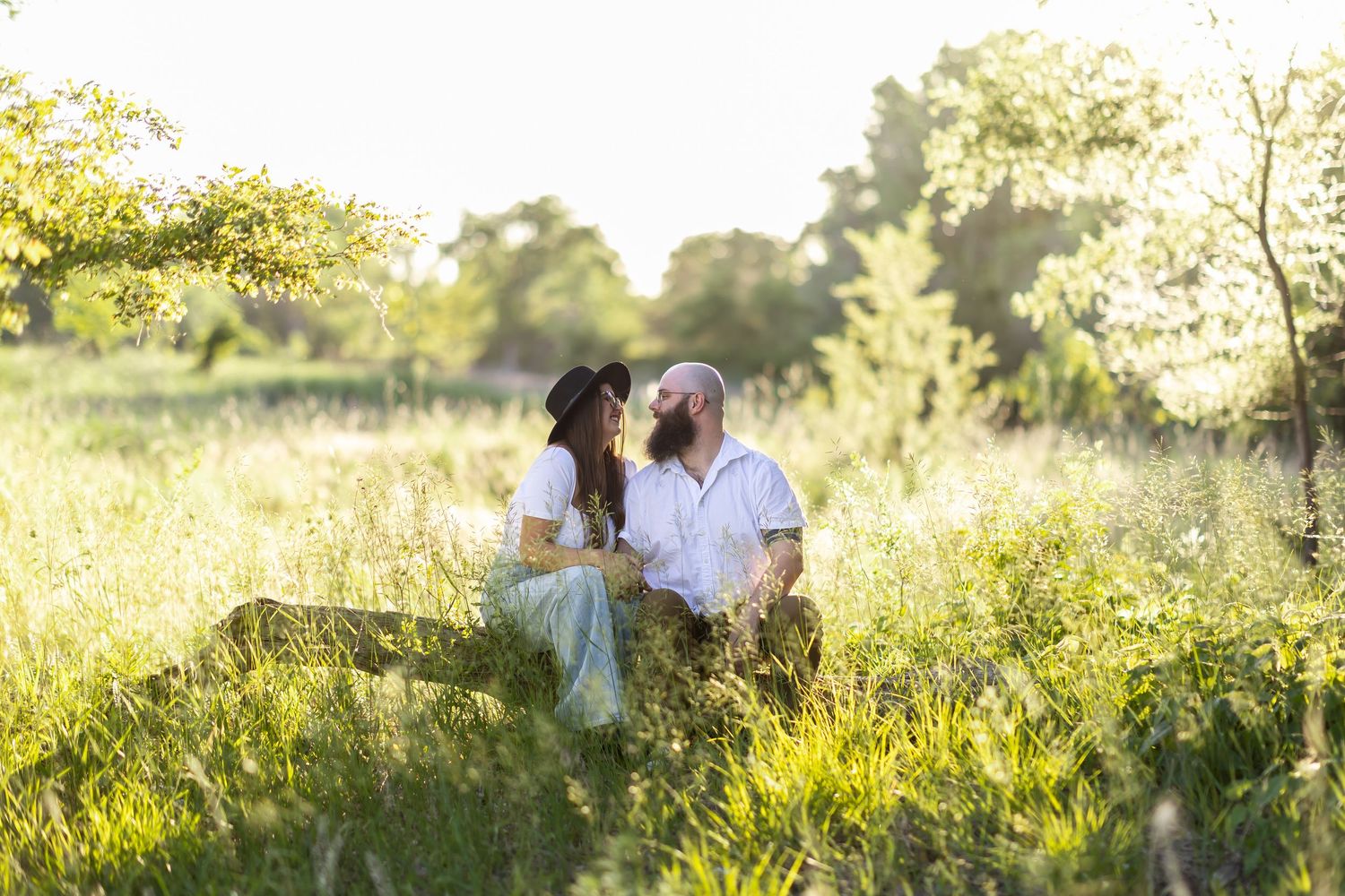 Romantic couple sitting together in a sun-drenched meadow during golden hour.