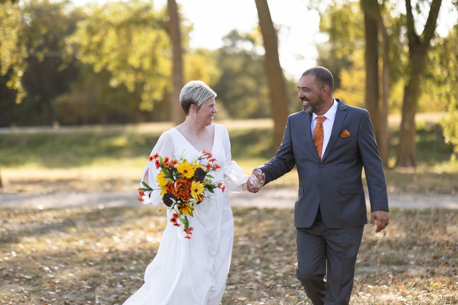 Newlywed couple walking together during golden hour with bride holding vibrant orange and yellow bouquet.